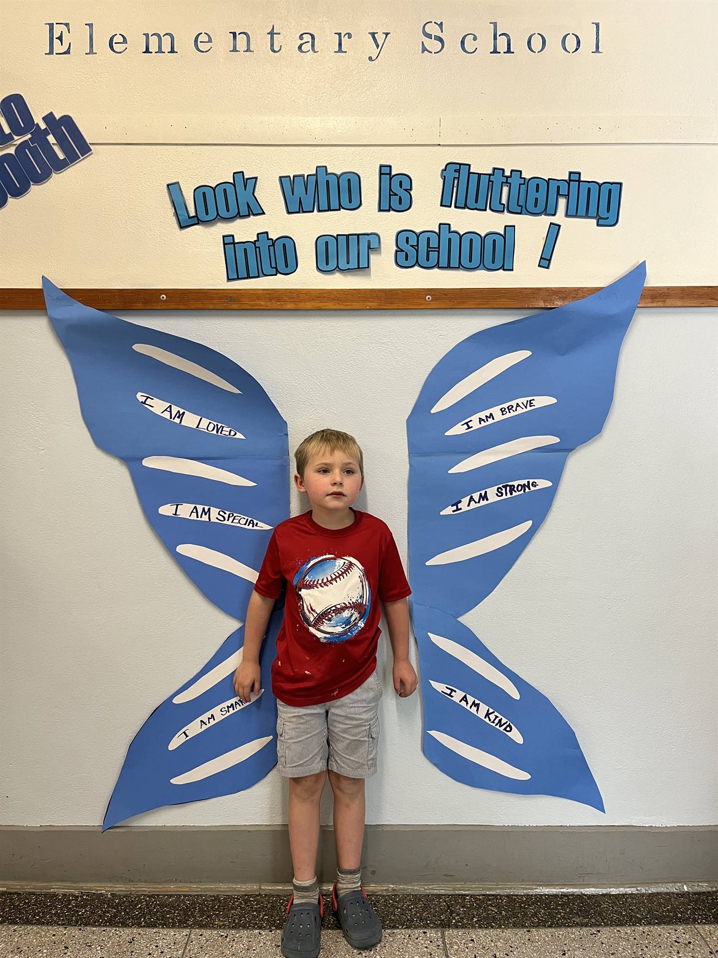 student standing between butterfly wings with sign on top saying "look who is fluttering into our sc