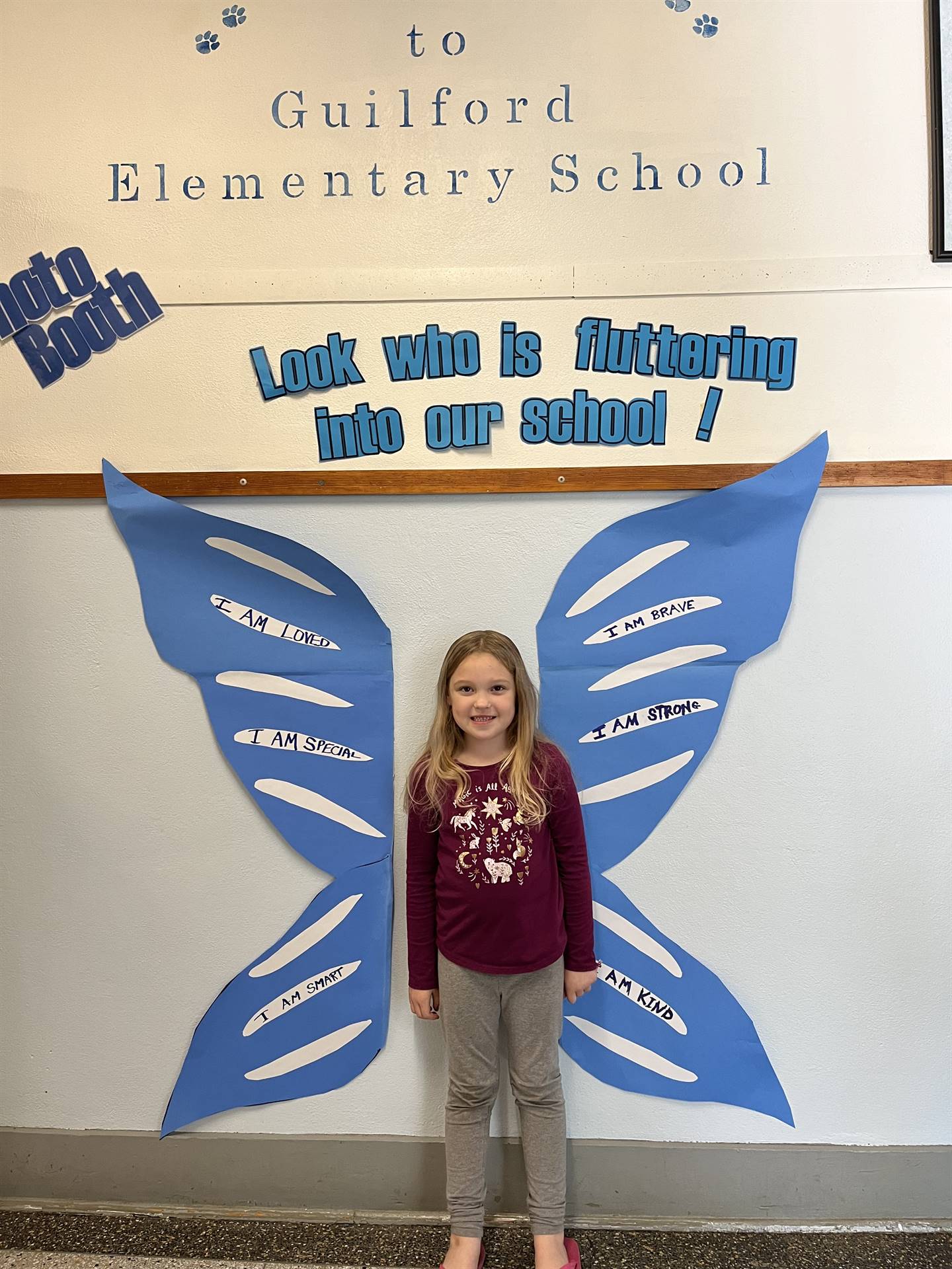 student standing between butterfly wings with sign on top saying "look who is fluttering into our sc