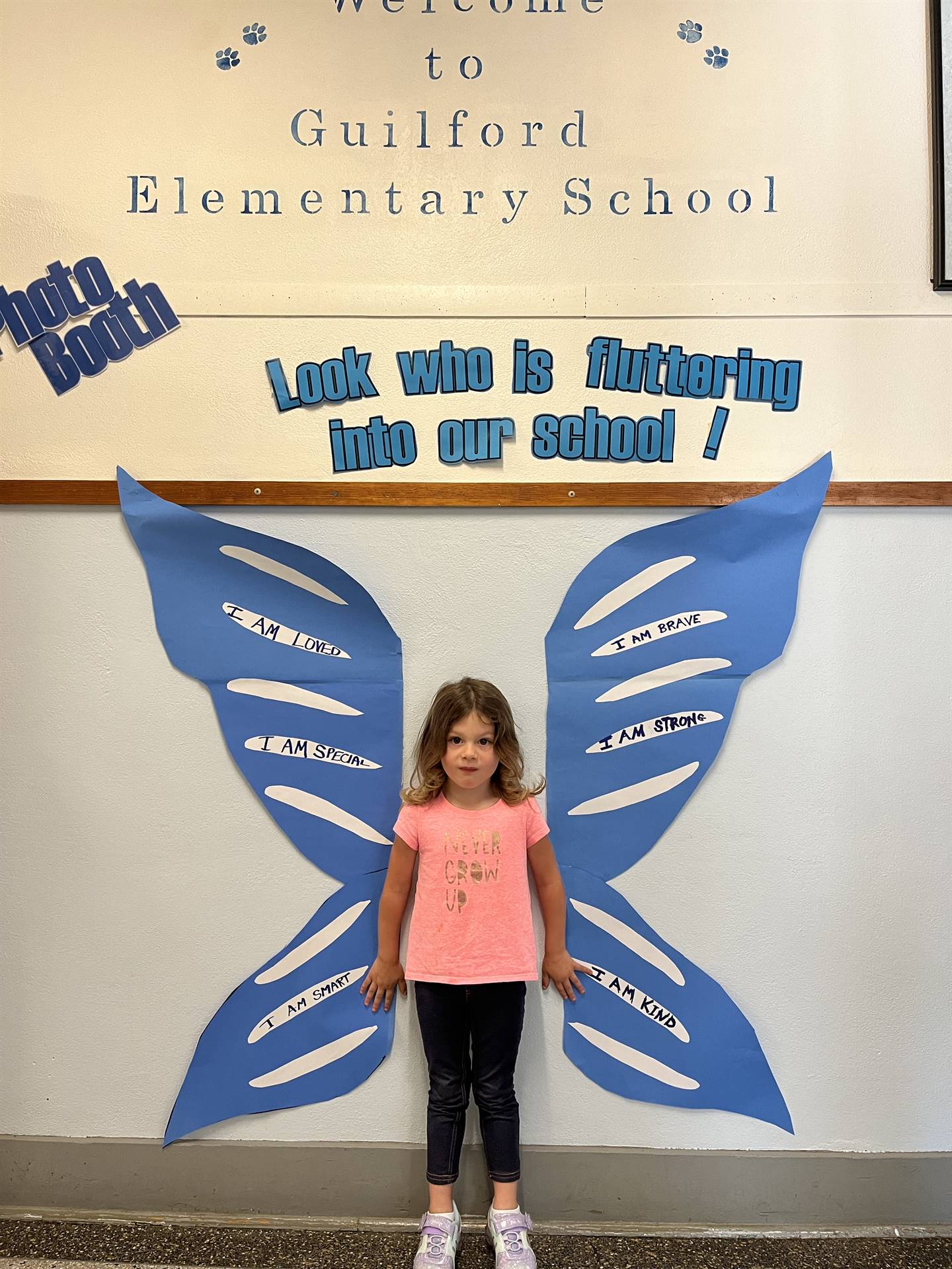 student standing between butterfly wings with sign on top saying "look who is fluttering into our sc