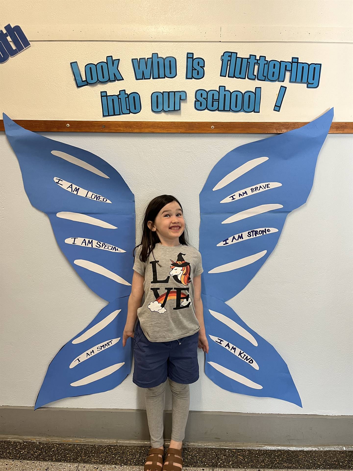 student standing between butterfly wings with sign on top saying "look who is fluttering into our sc