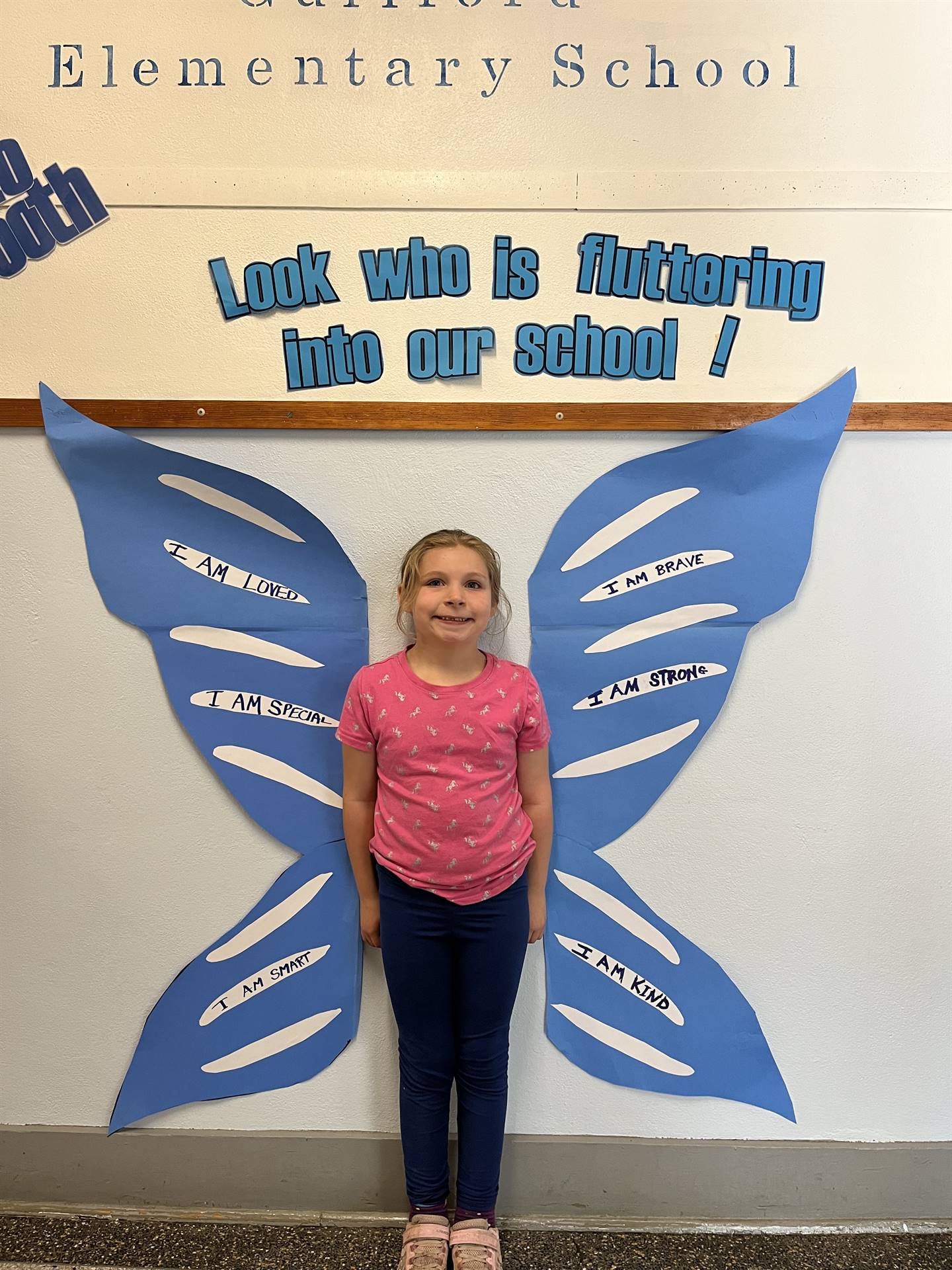 student standing between butterfly wings with sign on top saying "look who is fluttering into our sc