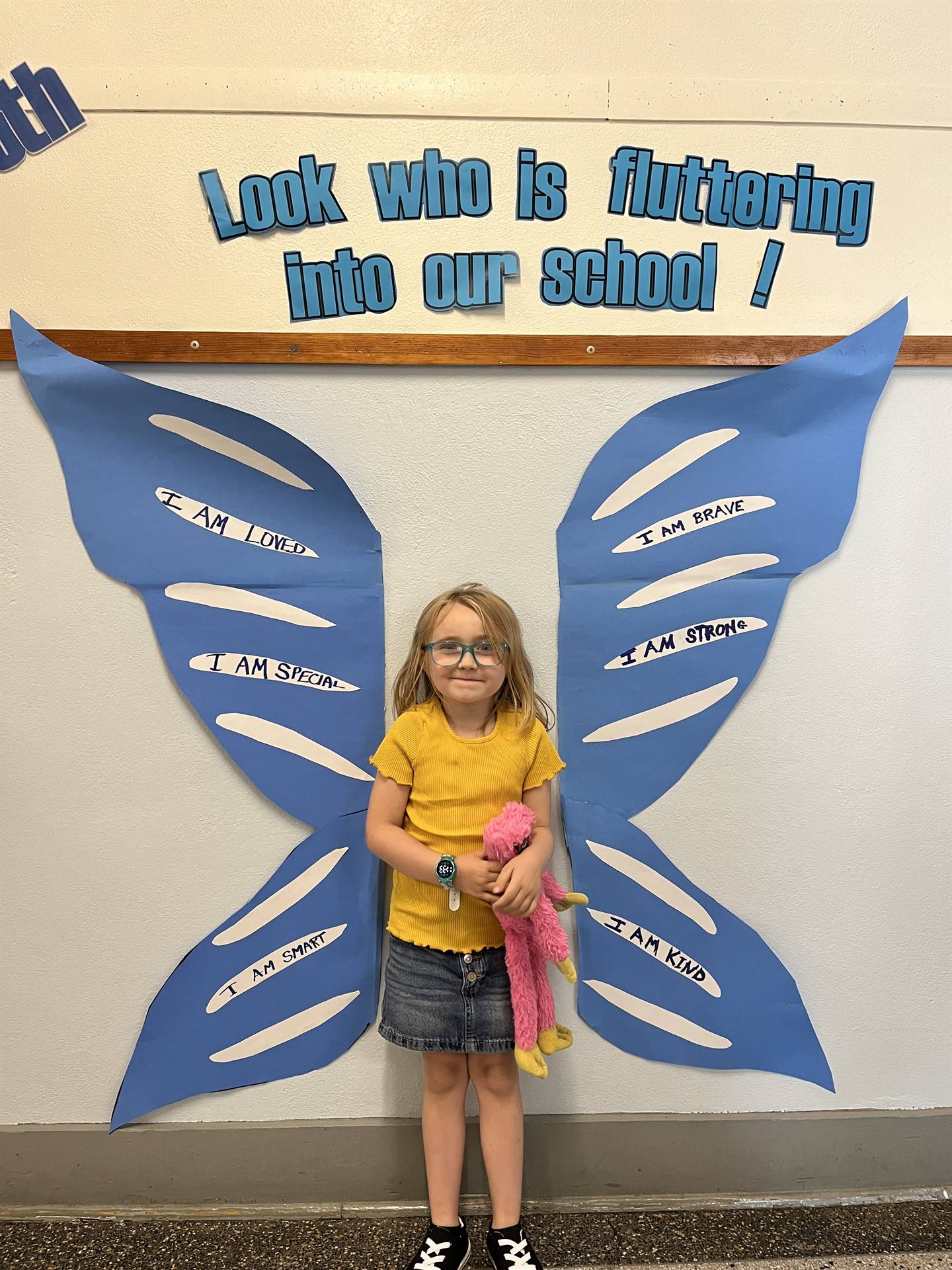 student standing between butterfly wings with sign on top saying "look who is fluttering into our sc