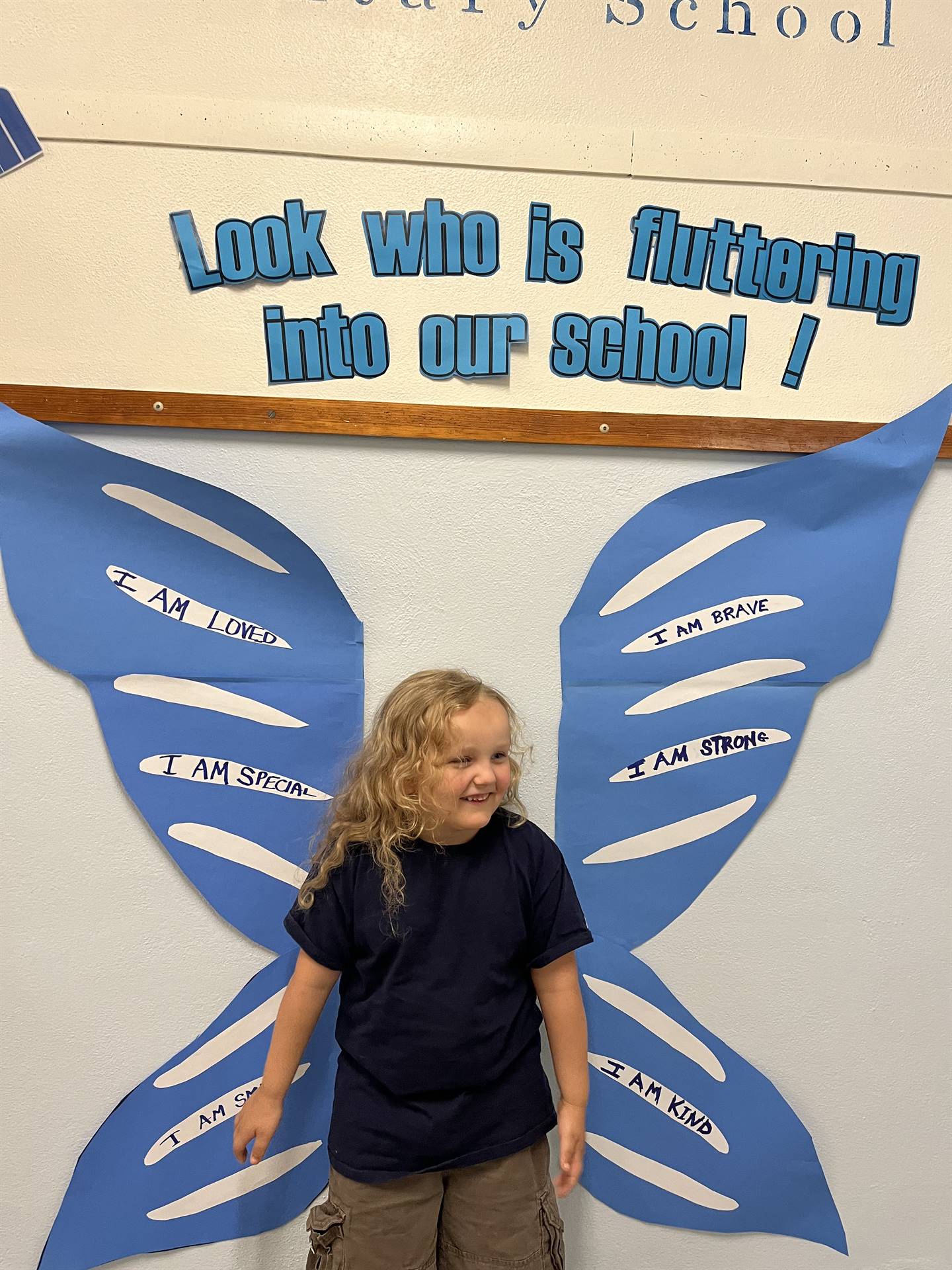 student standing between butterfly wings with sign on top saying "look who is fluttering into our sc