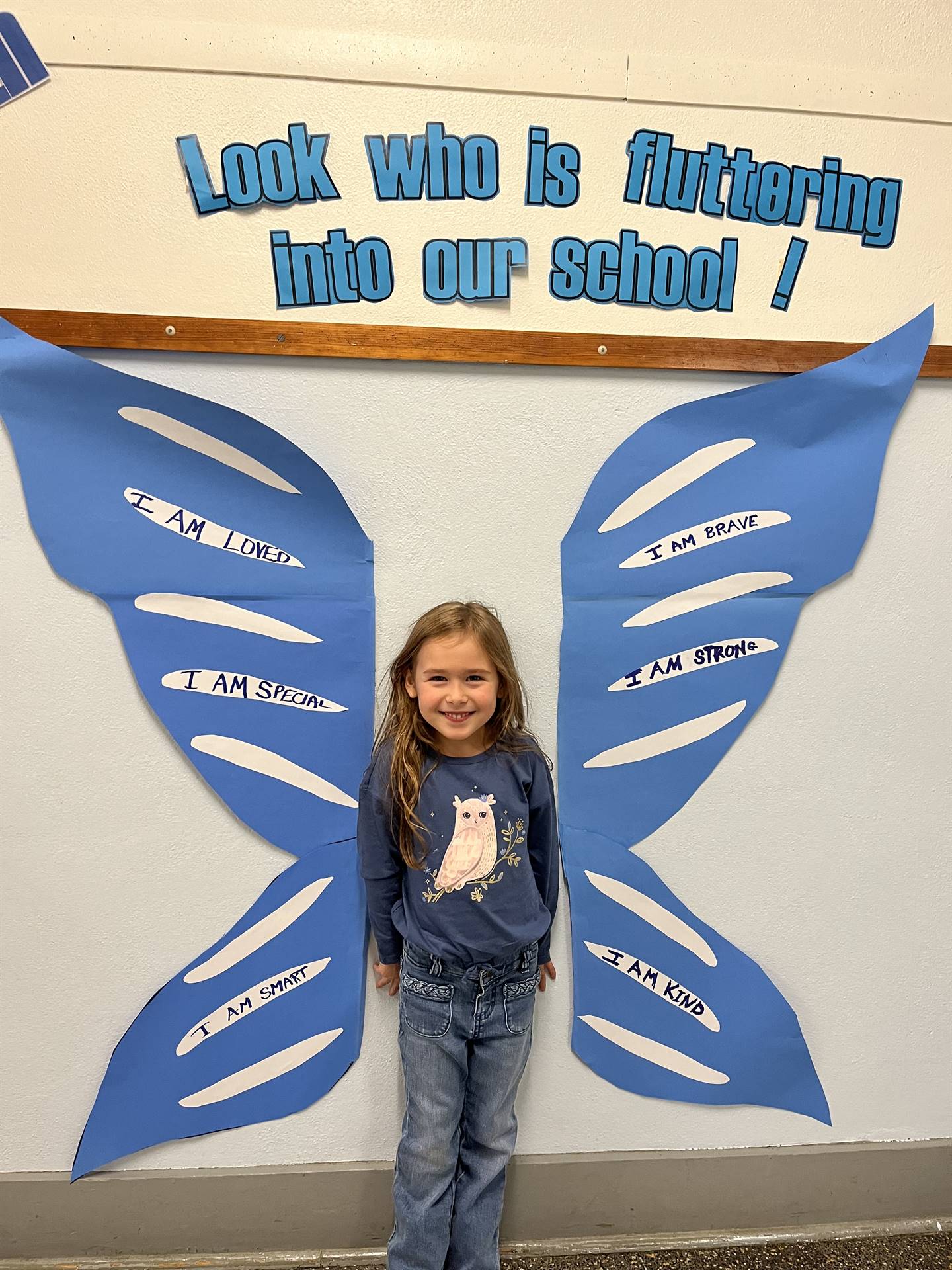 student standing between butterfly wings with sign on top saying "look who is fluttering into our sc