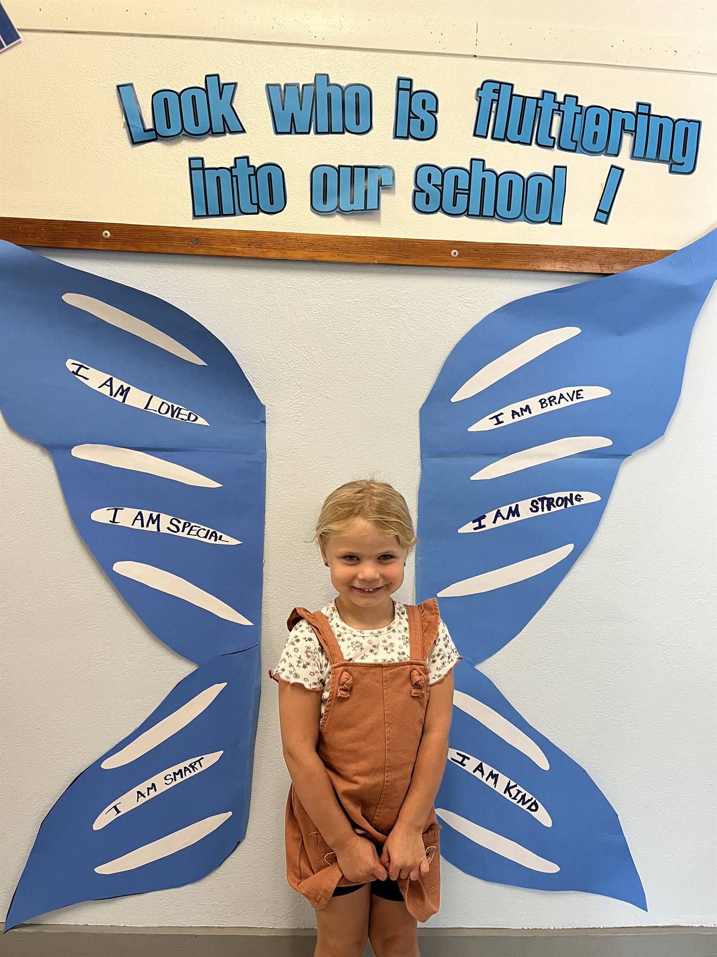 student standing between butterfly wings with sign on top saying "look who is fluttering into our sc