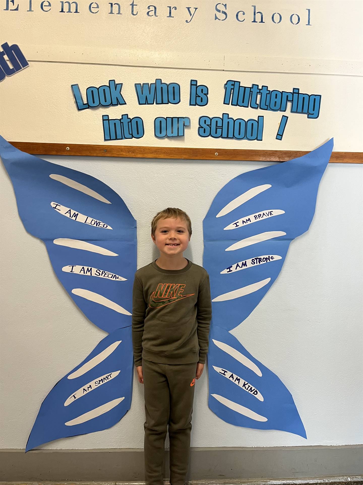 student standing between butterfly wings with sign on top saying "look who is fluttering into our sc