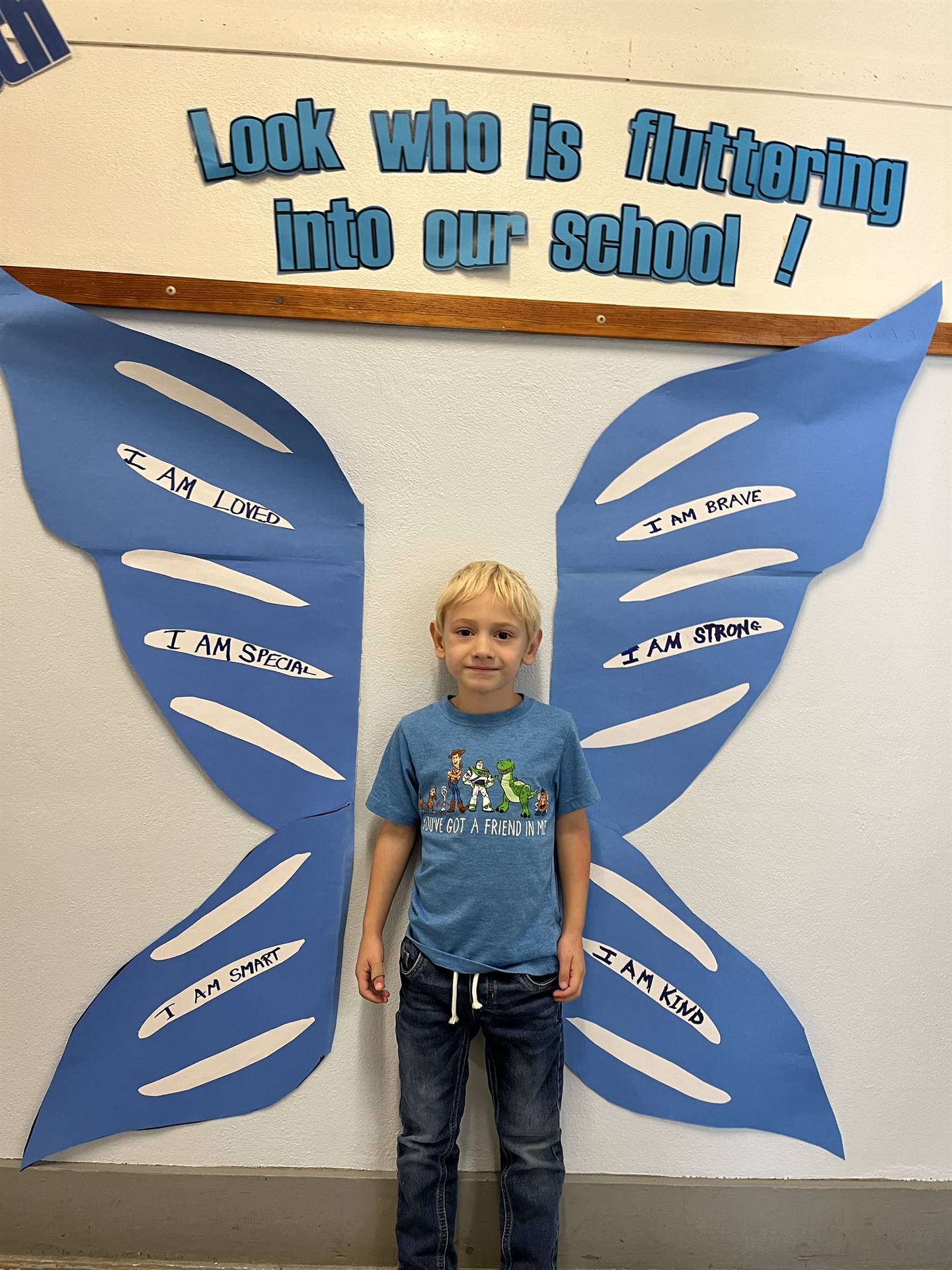 student standing between butterfly wings with sign on top saying "look who is fluttering into our sc