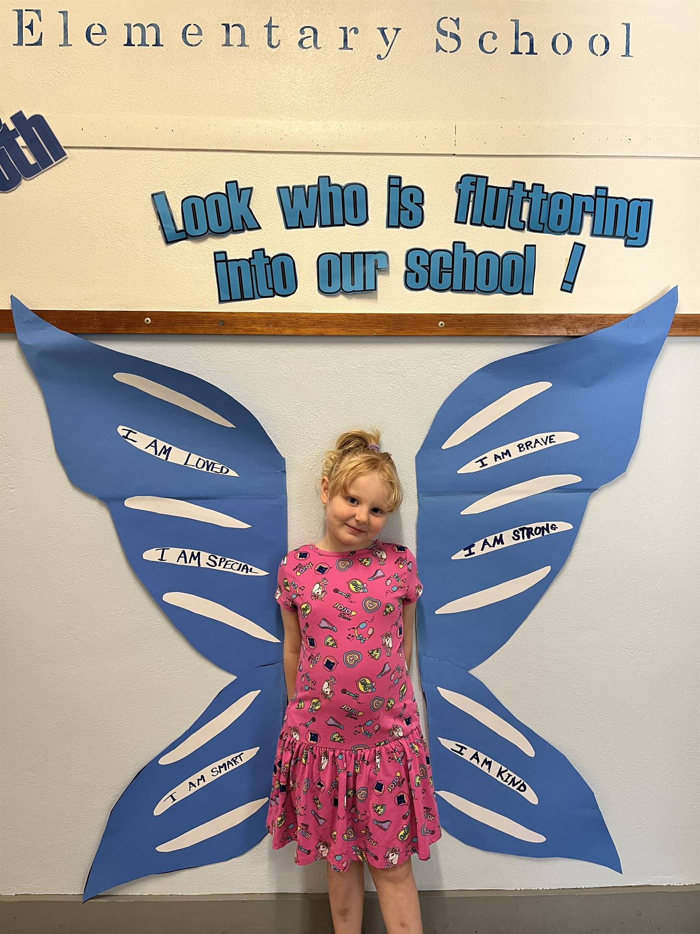 student standing between butterfly wings with sign on top saying "look who is fluttering into our sc