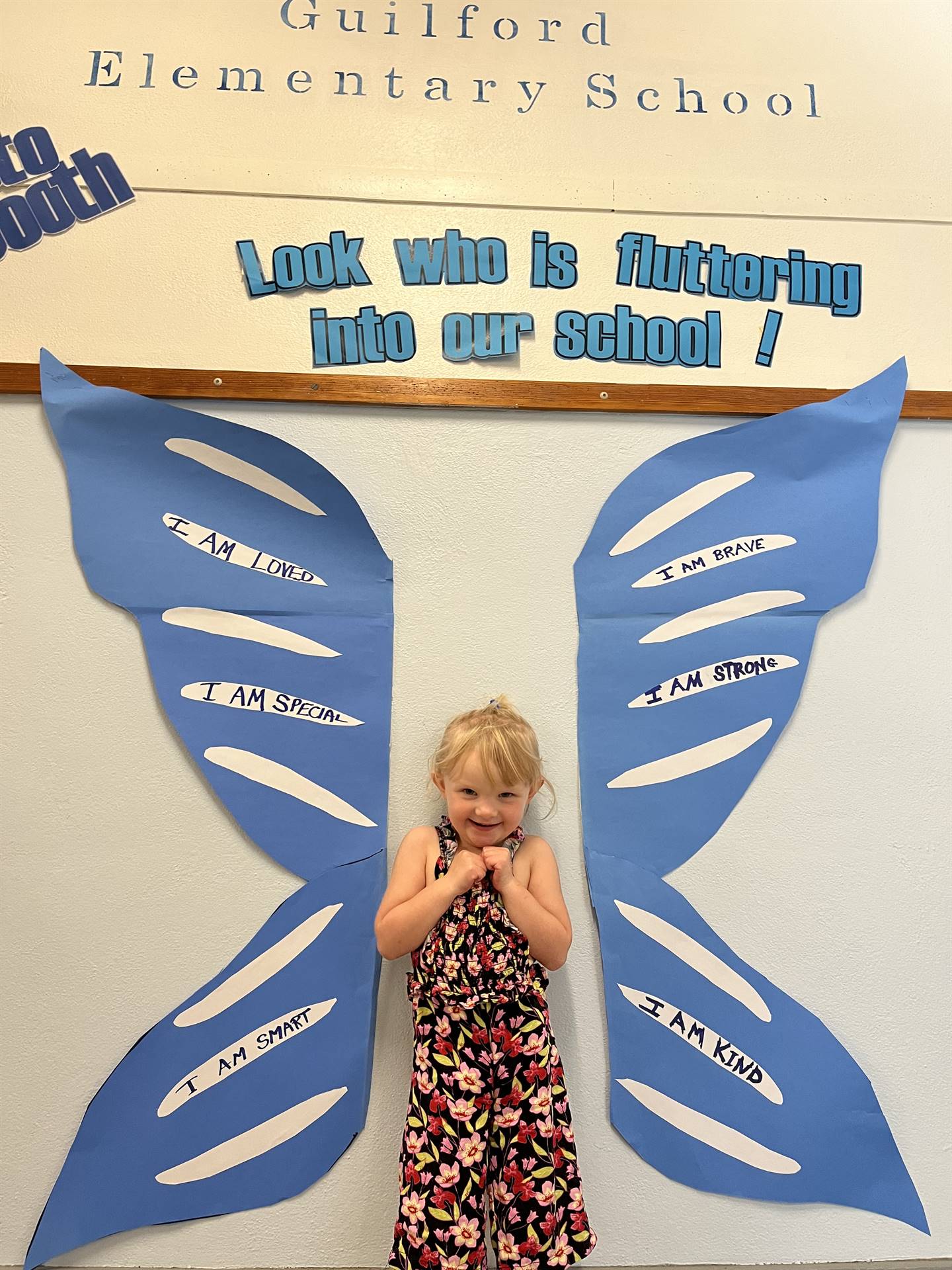 student standing between butterfly wings with sign on top saying "look who is fluttering into our sc