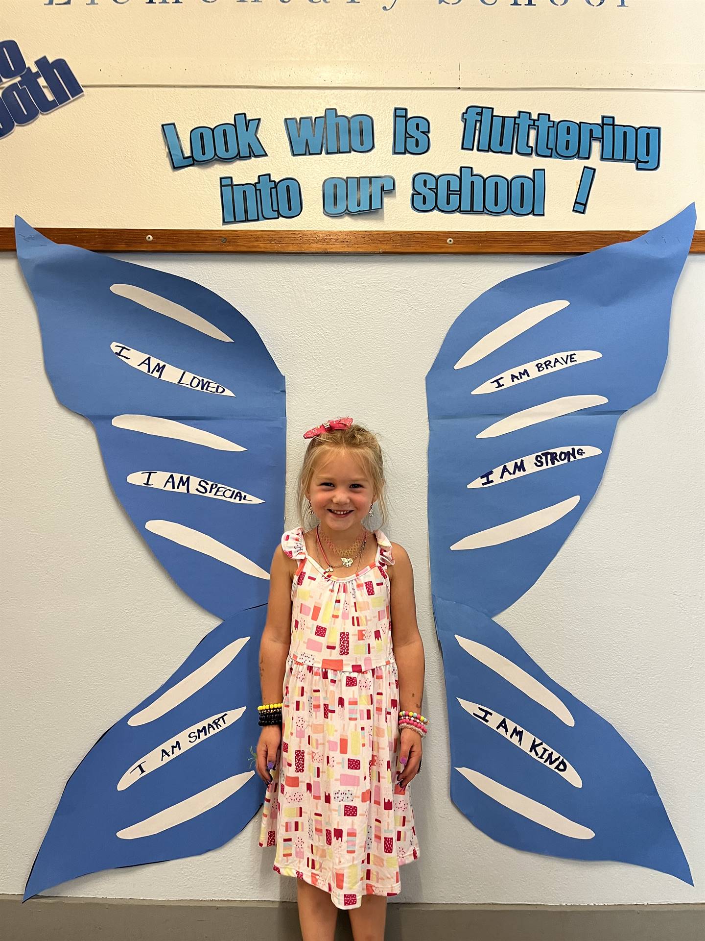 student standing between butterfly wings with sign on top saying "look who is fluttering into our sc