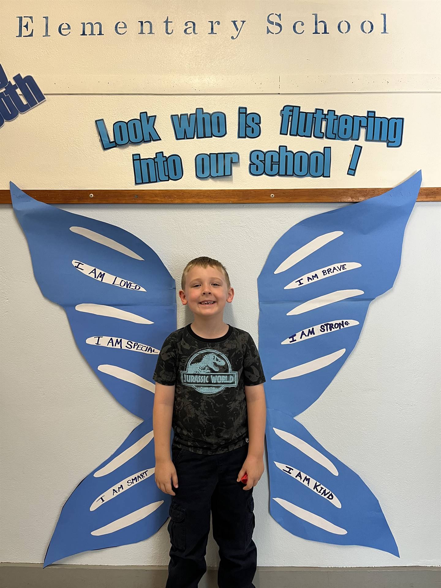 student standing between butterfly wings with sign on top saying "look who is fluttering into our sc