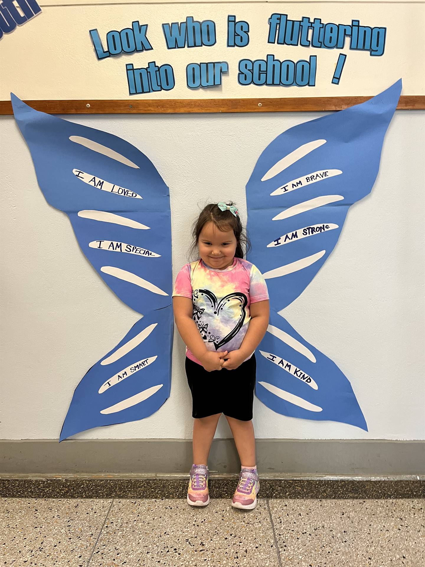 student standing between butterfly wings with sign on top saying "look who is fluttering into our sc