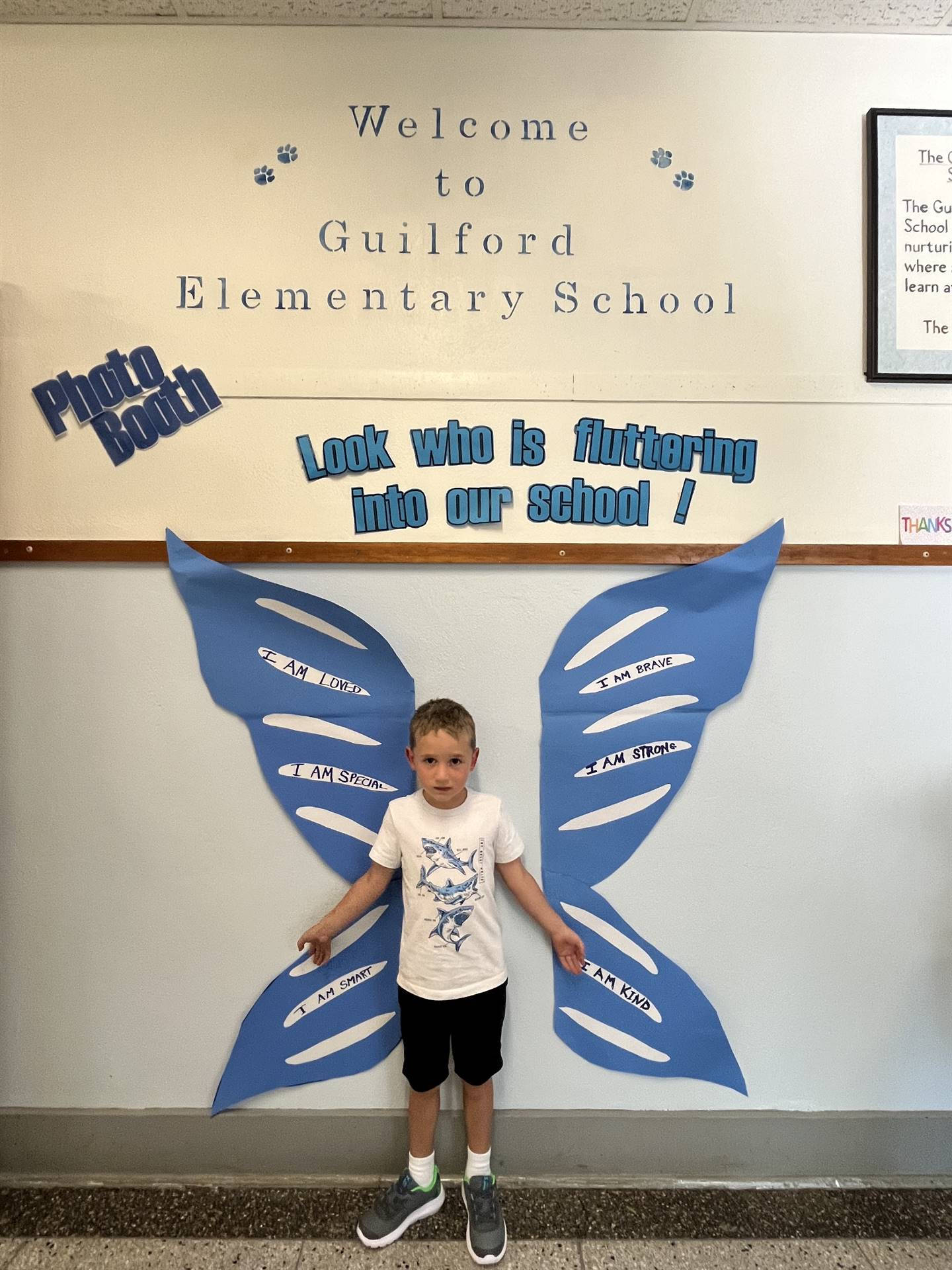 student standing between butterfly wings with sign on top saying "look who is fluttering into our sc