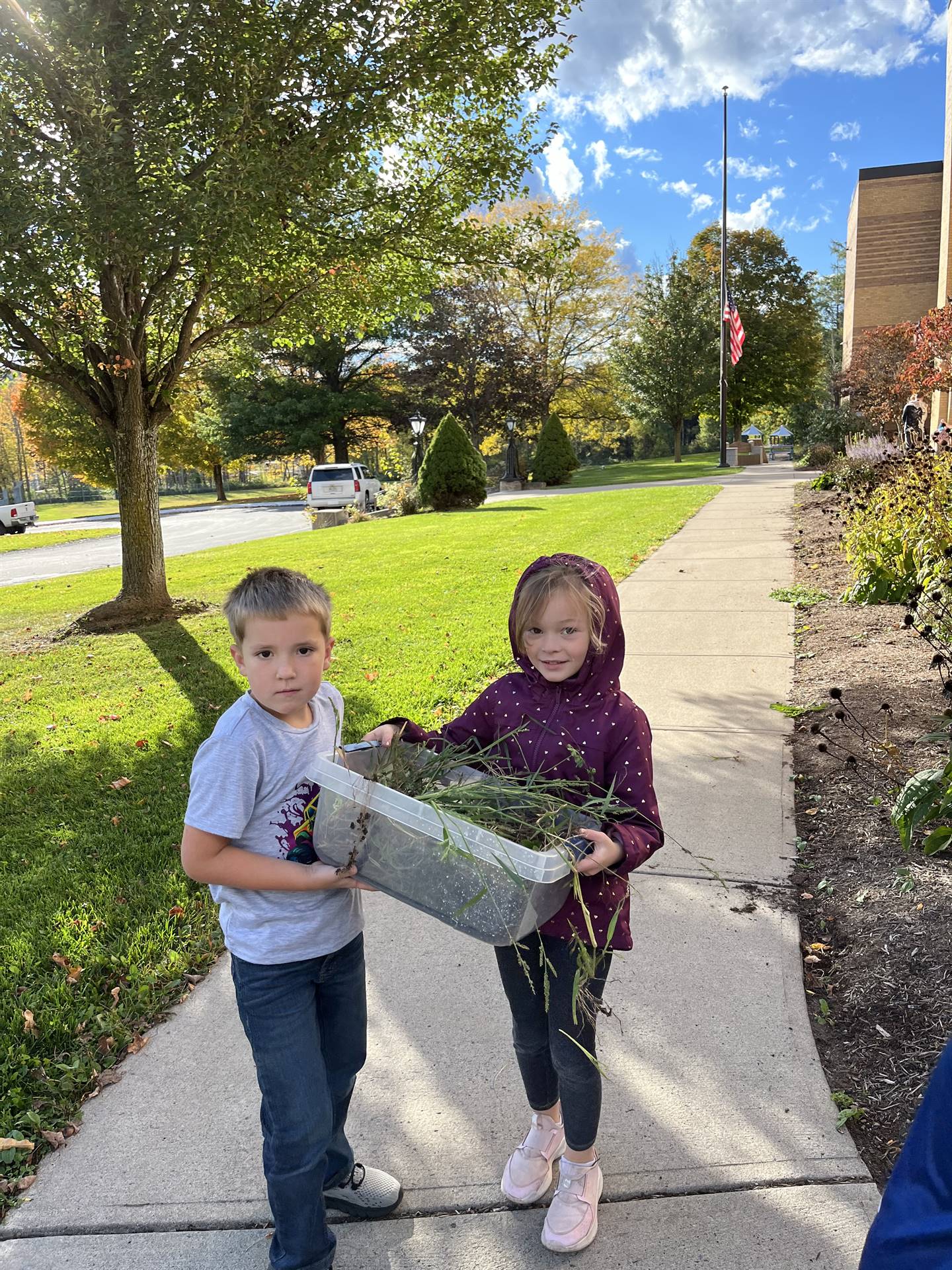 2 students carrying a container of weeds.