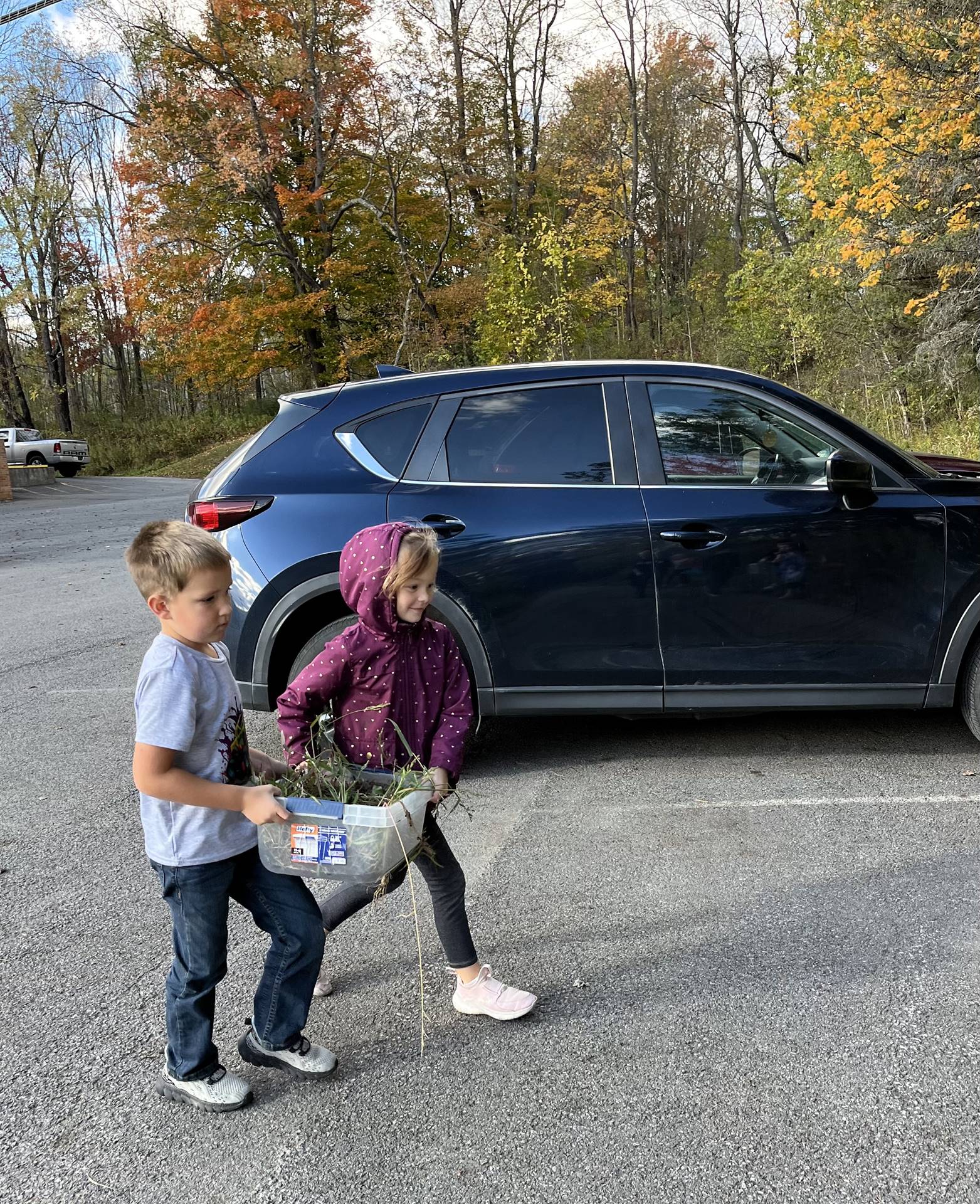 2 students carrying a container of weeds.