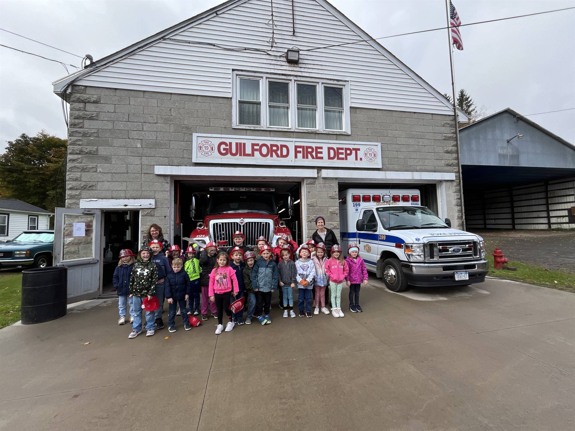A group of students stand in front of fire truck and an ambulance is in the garage to the right