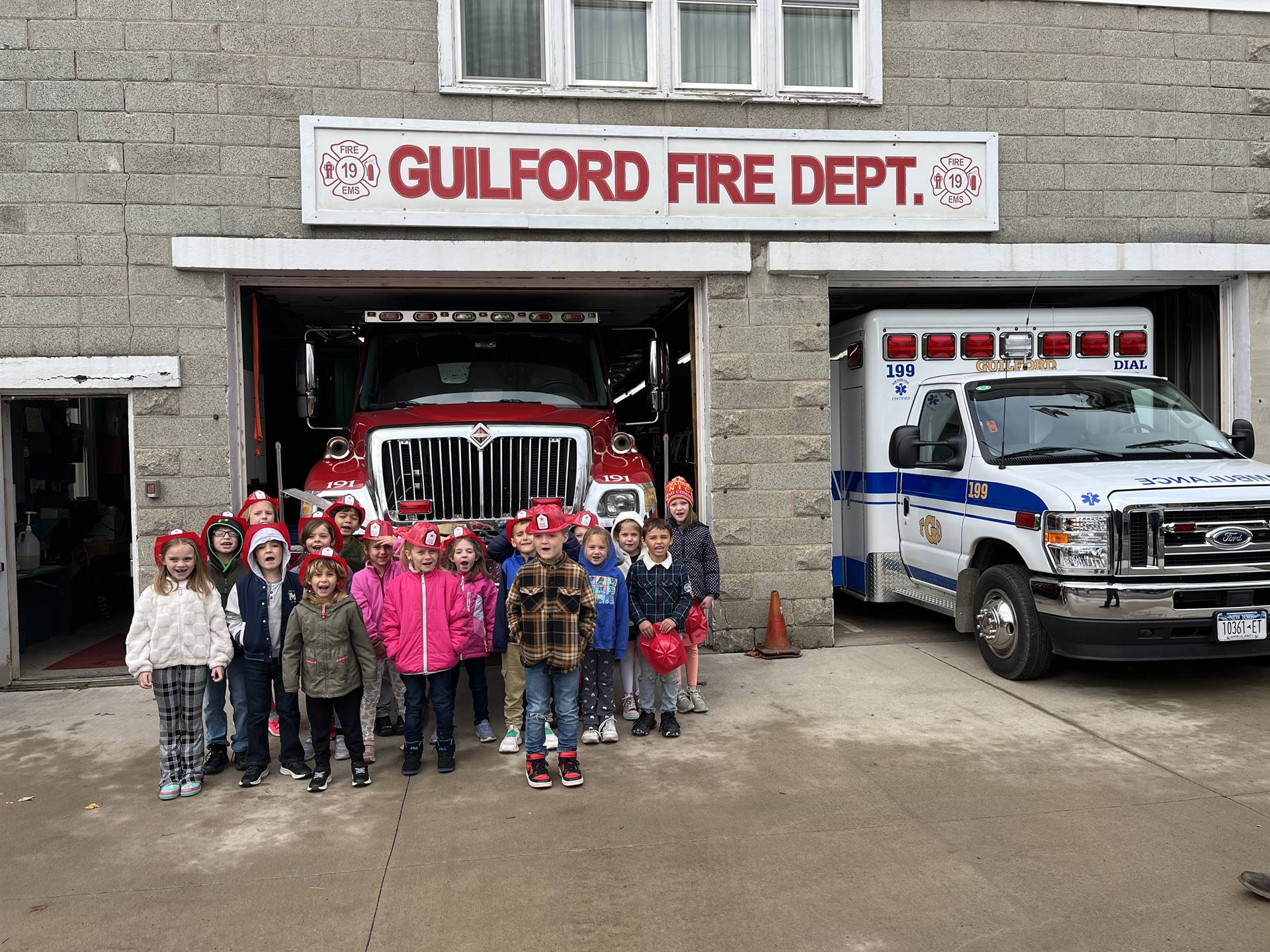 A group of students stand in front of fire truck and an ambulance is in the garage to the right