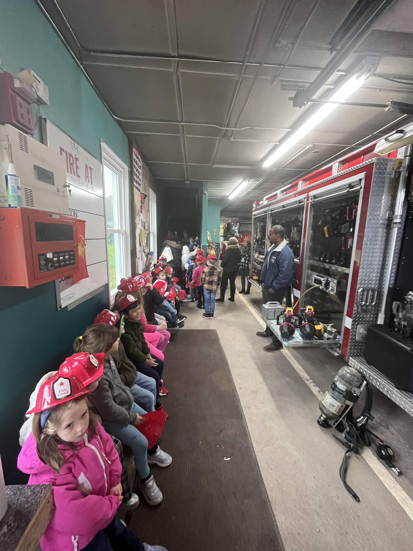 students sit inside a firehouse next to a large fire engine