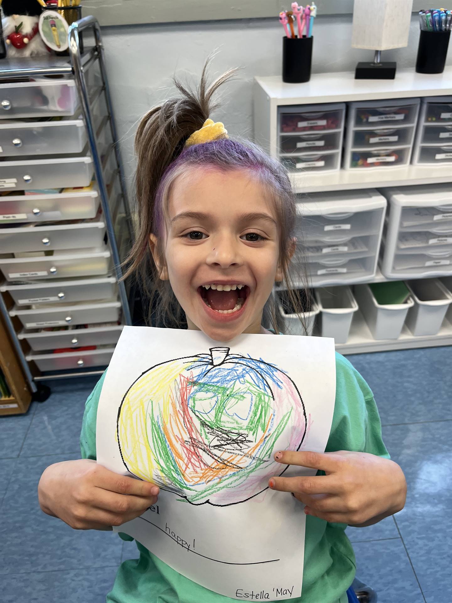 student holding a rainbow pumpkin face with a happy emotion