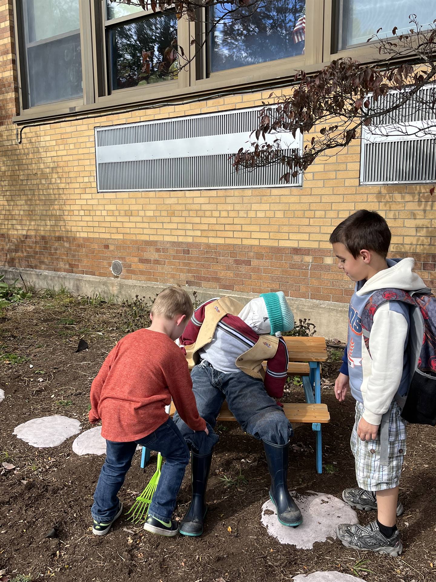 2 kids checking out a scarecrow on a bench.