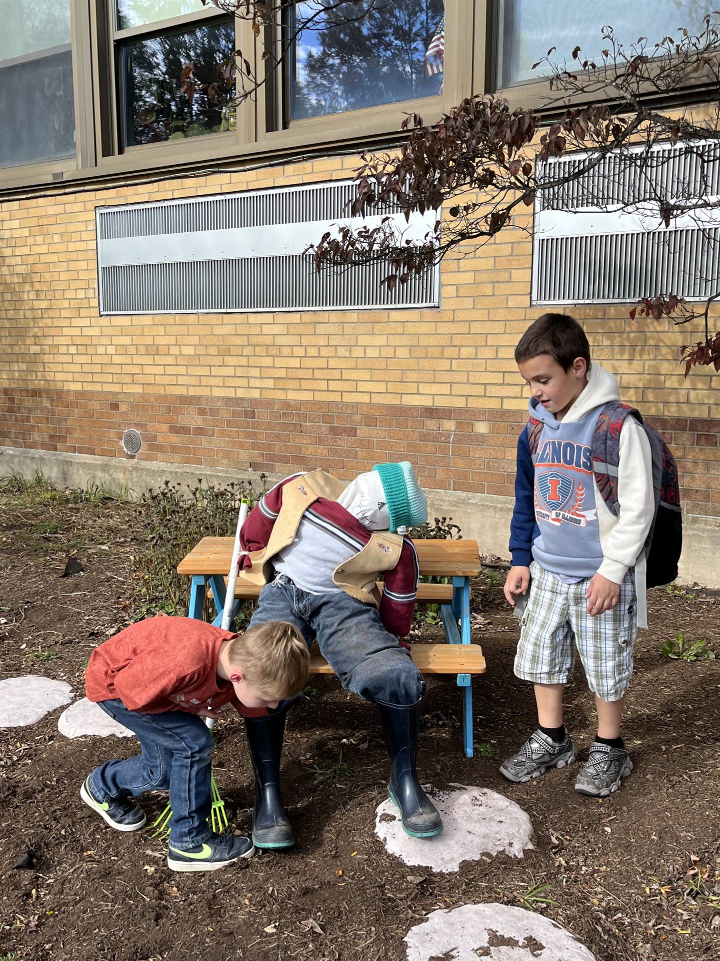 2 kids checking out a scarecrow on a bench.