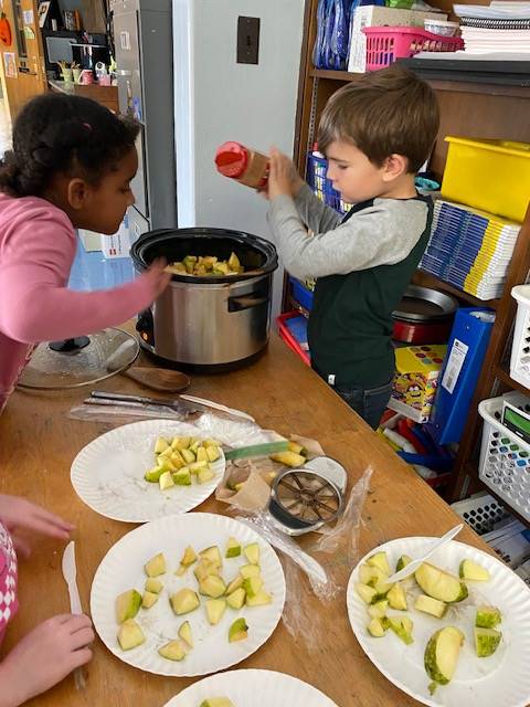 students putting apples into a crock pot and sprinkling cinnamon on top