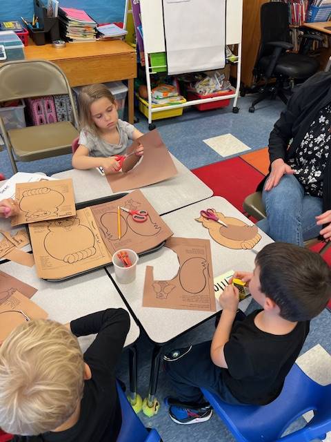 students at a table cutting out a shape from brown paper