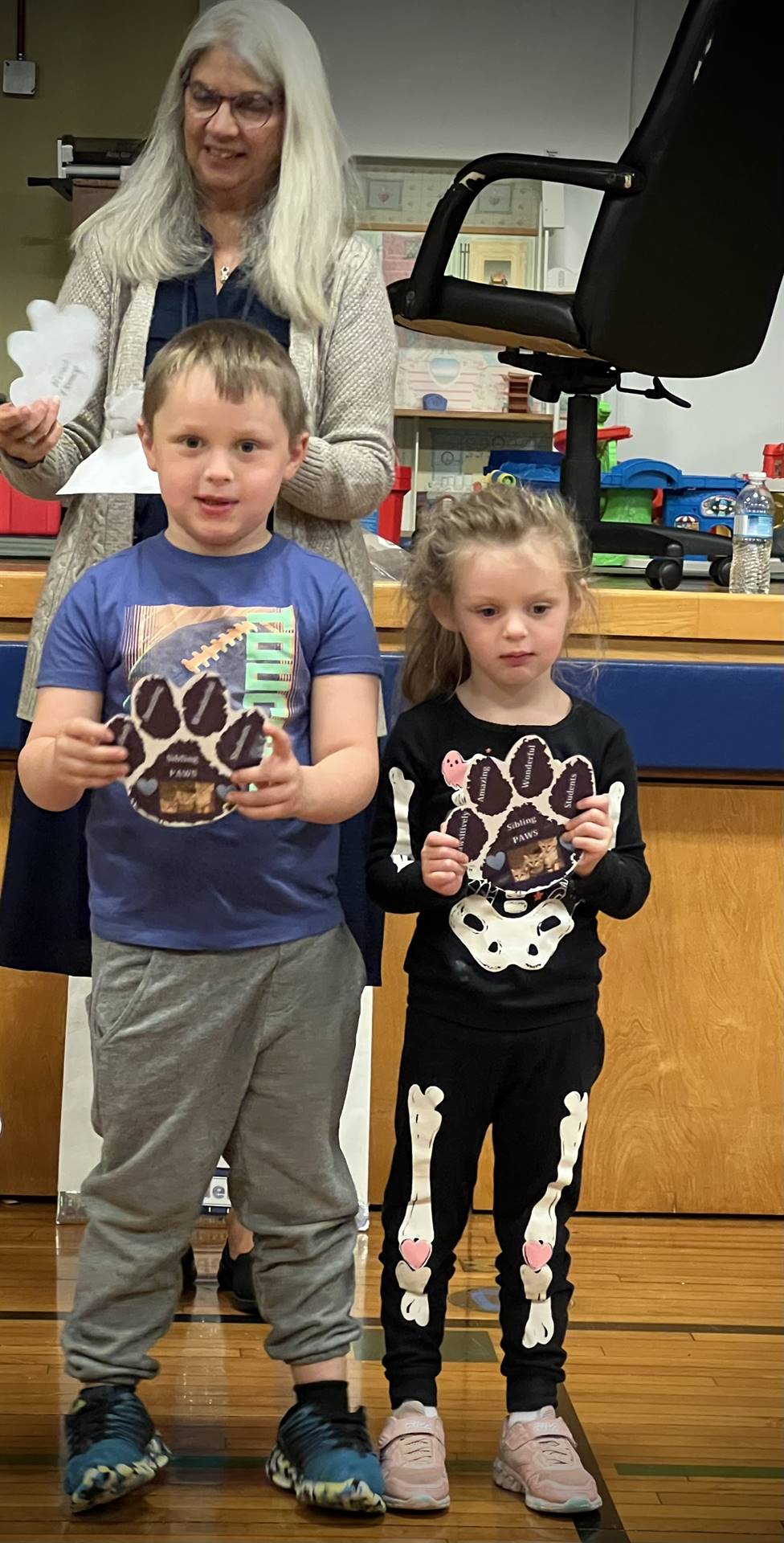 2 students holding a paper paw with adult in background