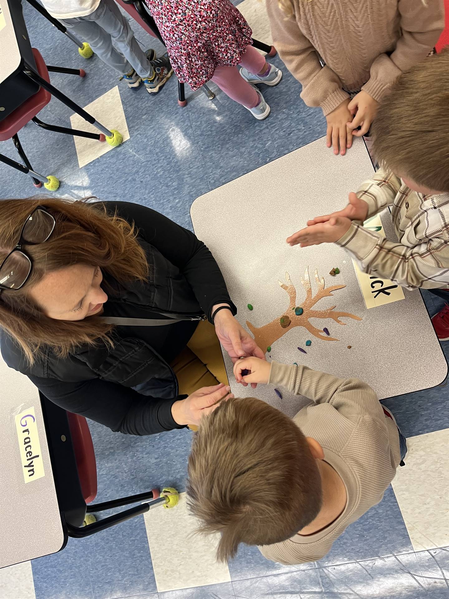 2 students and an adult using play do to create leaves for a bare fall tree