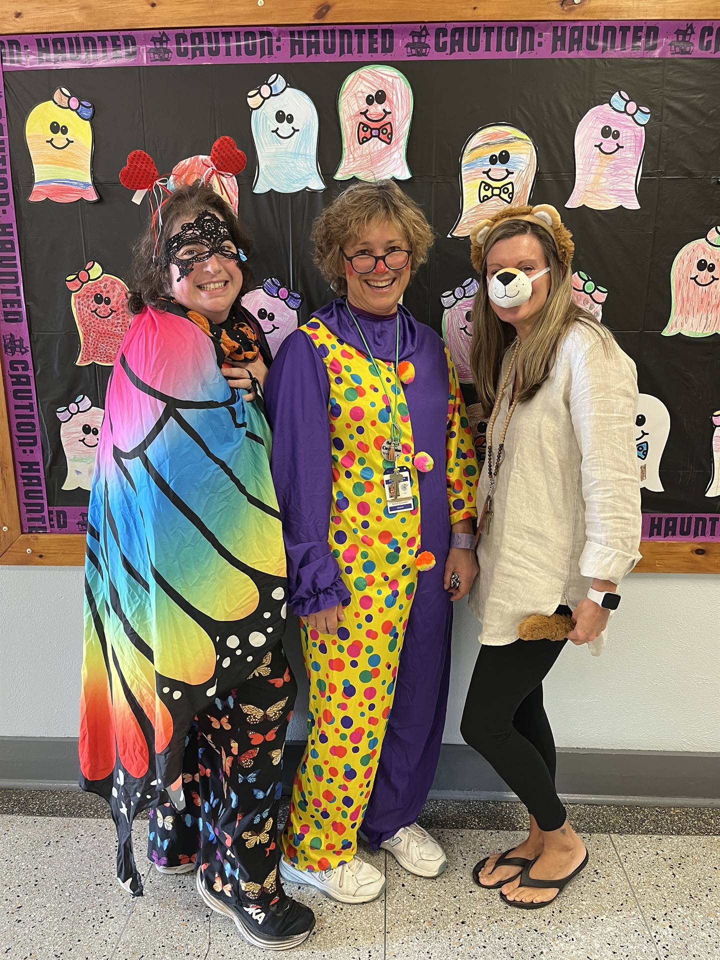 3 adults dressed in costumes with a ghostly bulletin board in backgroun