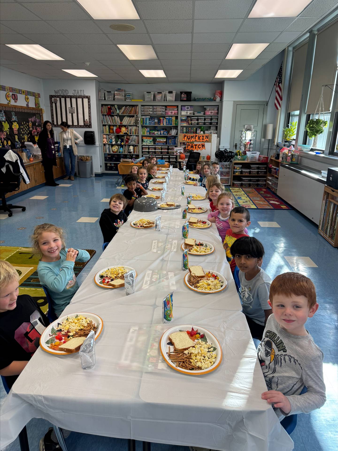children sitting at a long white covered table with plates of food.
