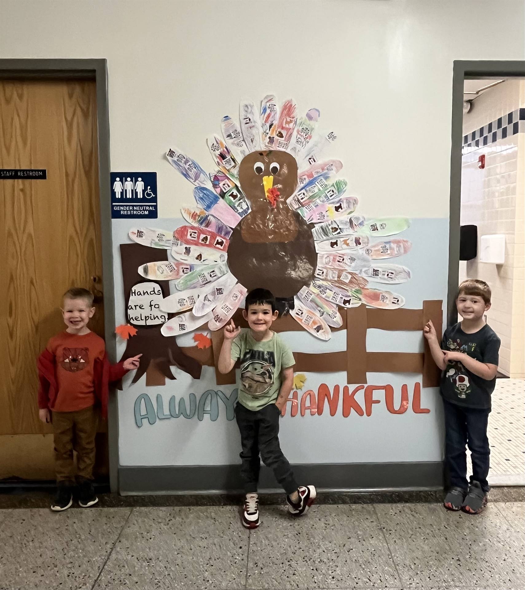 3 students with a Thankful Turkey on the wall behind them 