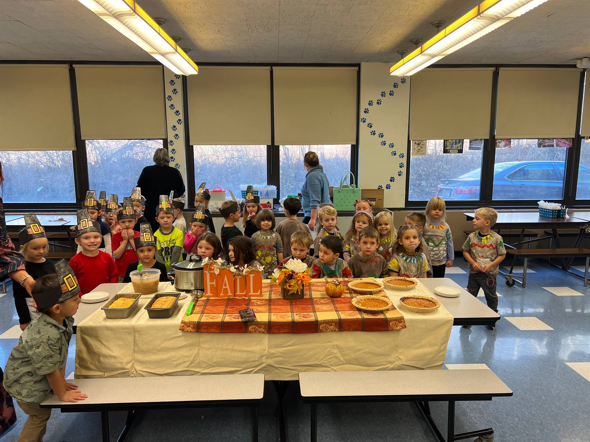 Children dressed as pilgrims and native americans gathered around a table of food.