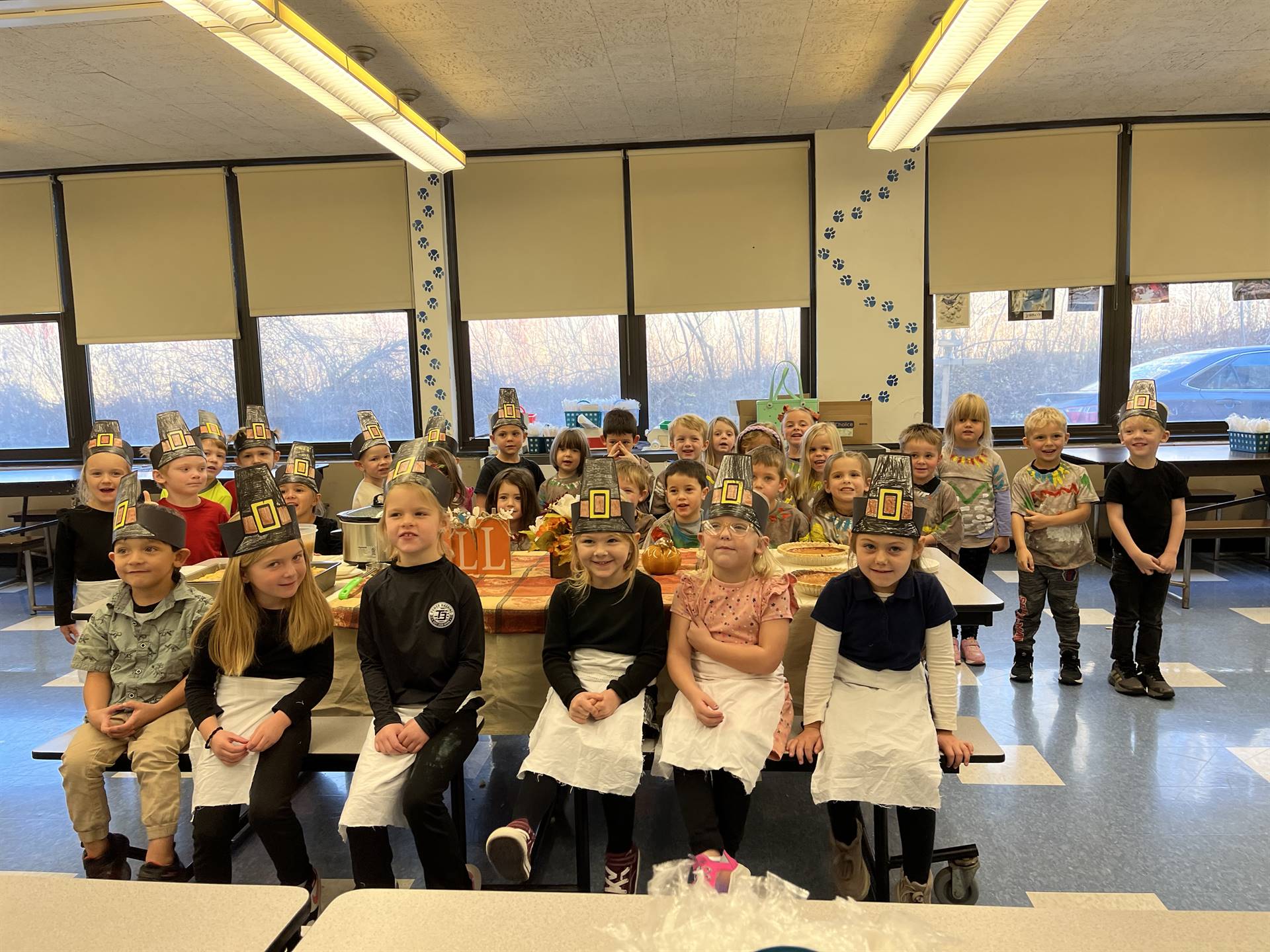 Children dressed as pilgrims and native americans gathered around a table of food.