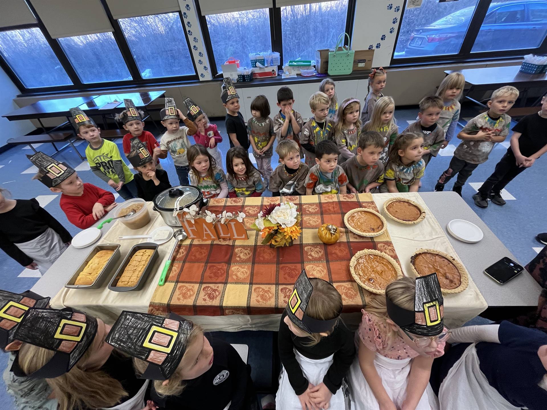 Children dressed as pilgrims and native americans gathered around a table of food.