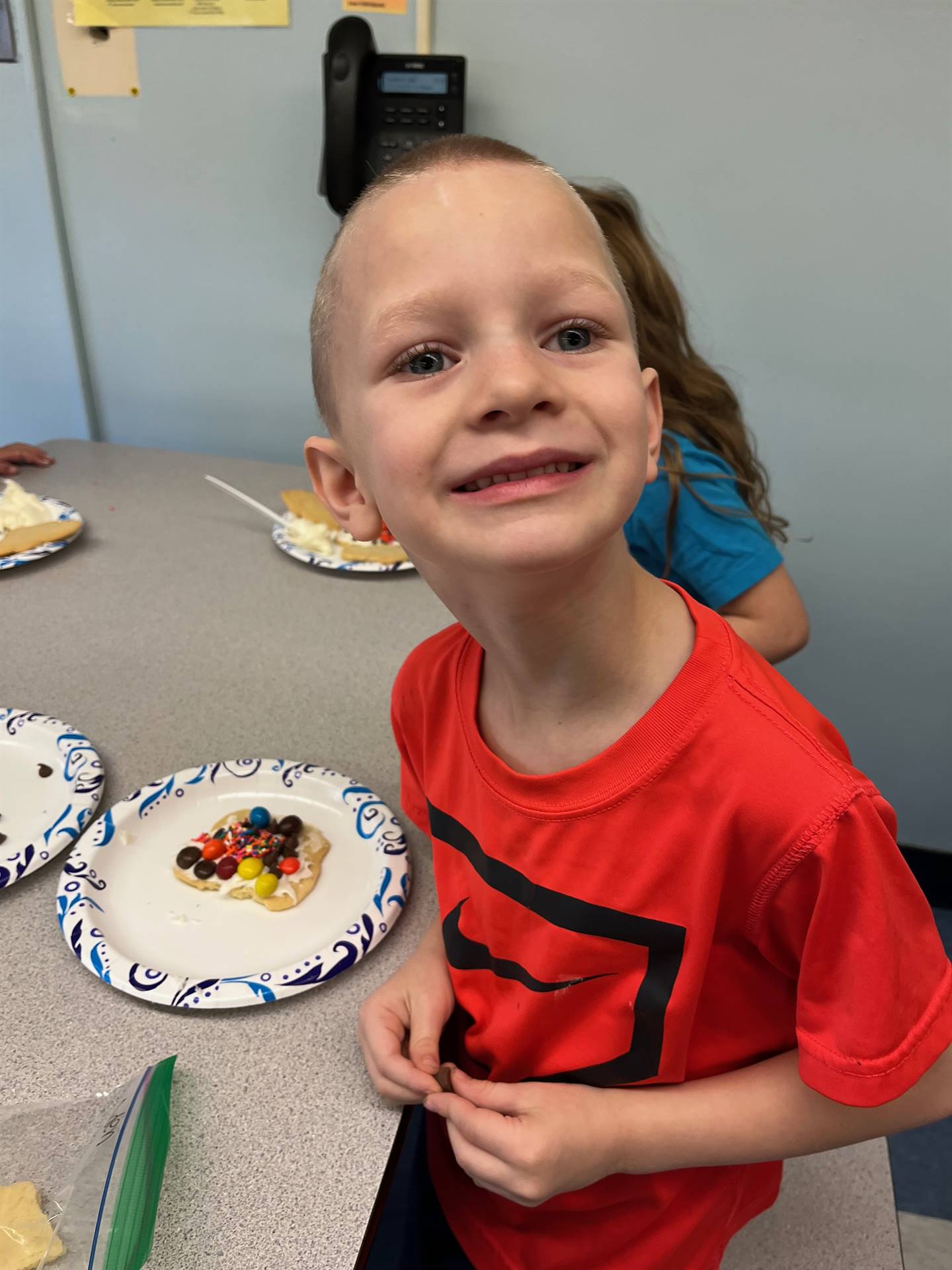 student smiling and decorating sugar cookie with icing and candy