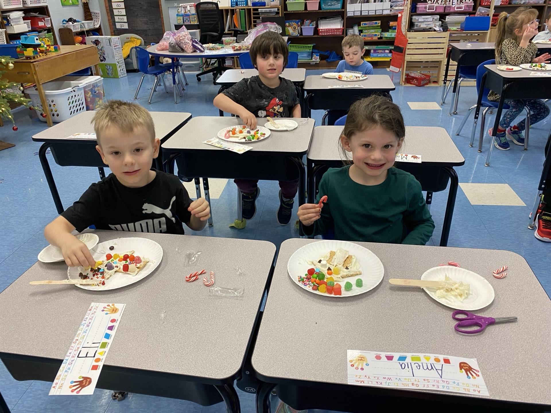 2 students with a decorated gingerbread house.