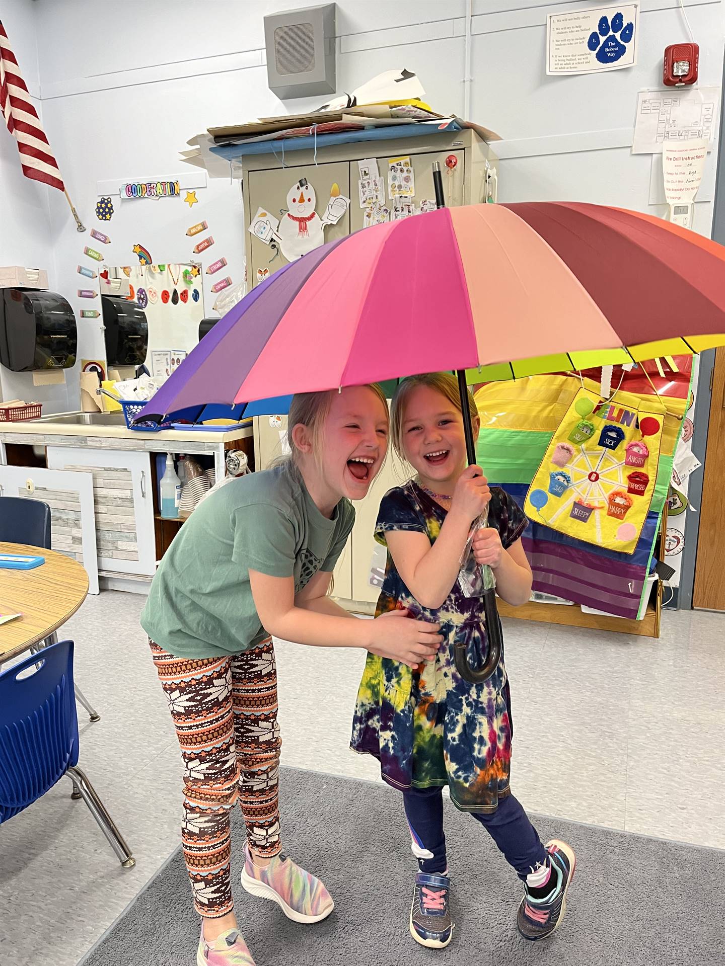 Students laughing under a rainbow colored umbrella.