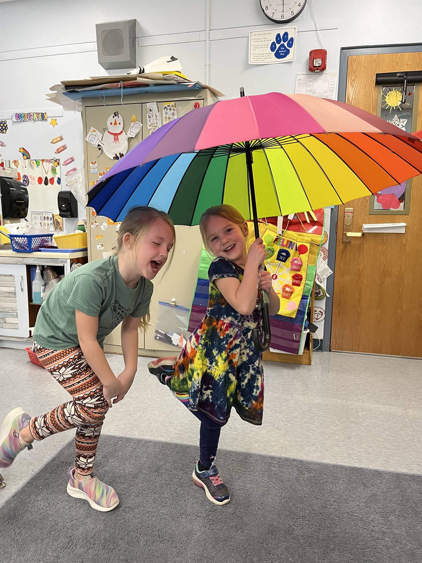 Students laughing under a rainbow colored umbrella.