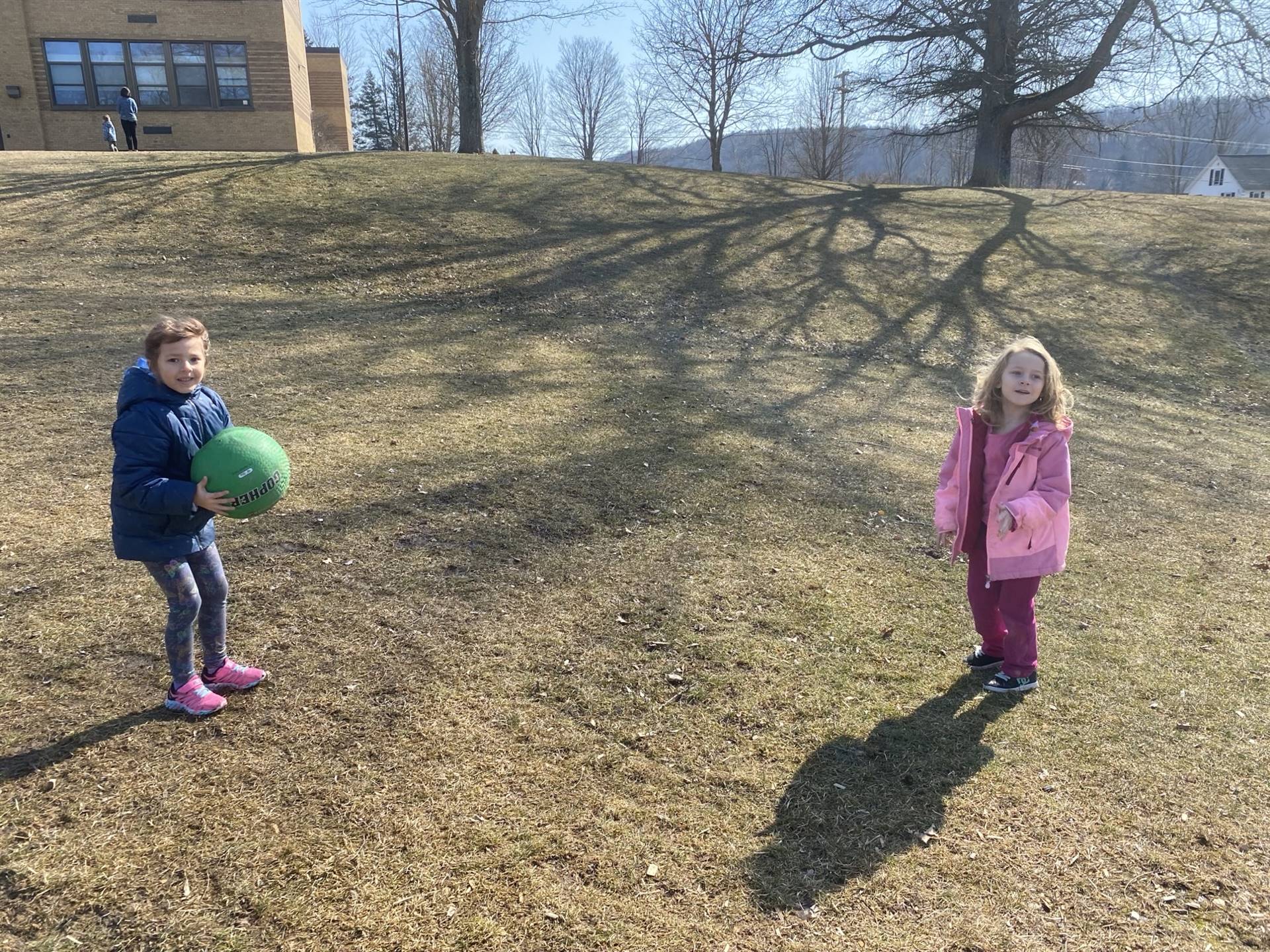 2 students playing toss with a ball outside