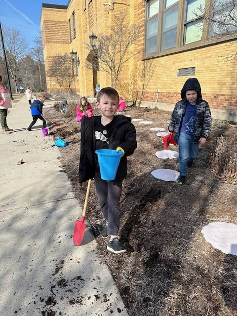 2 students on a dirt pile with a shovel and pail