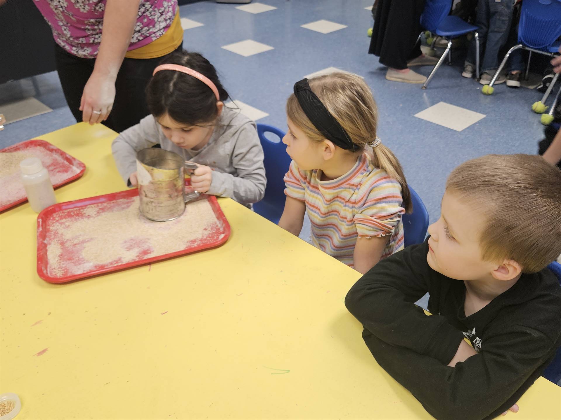 3 kids take turns sifting flour.