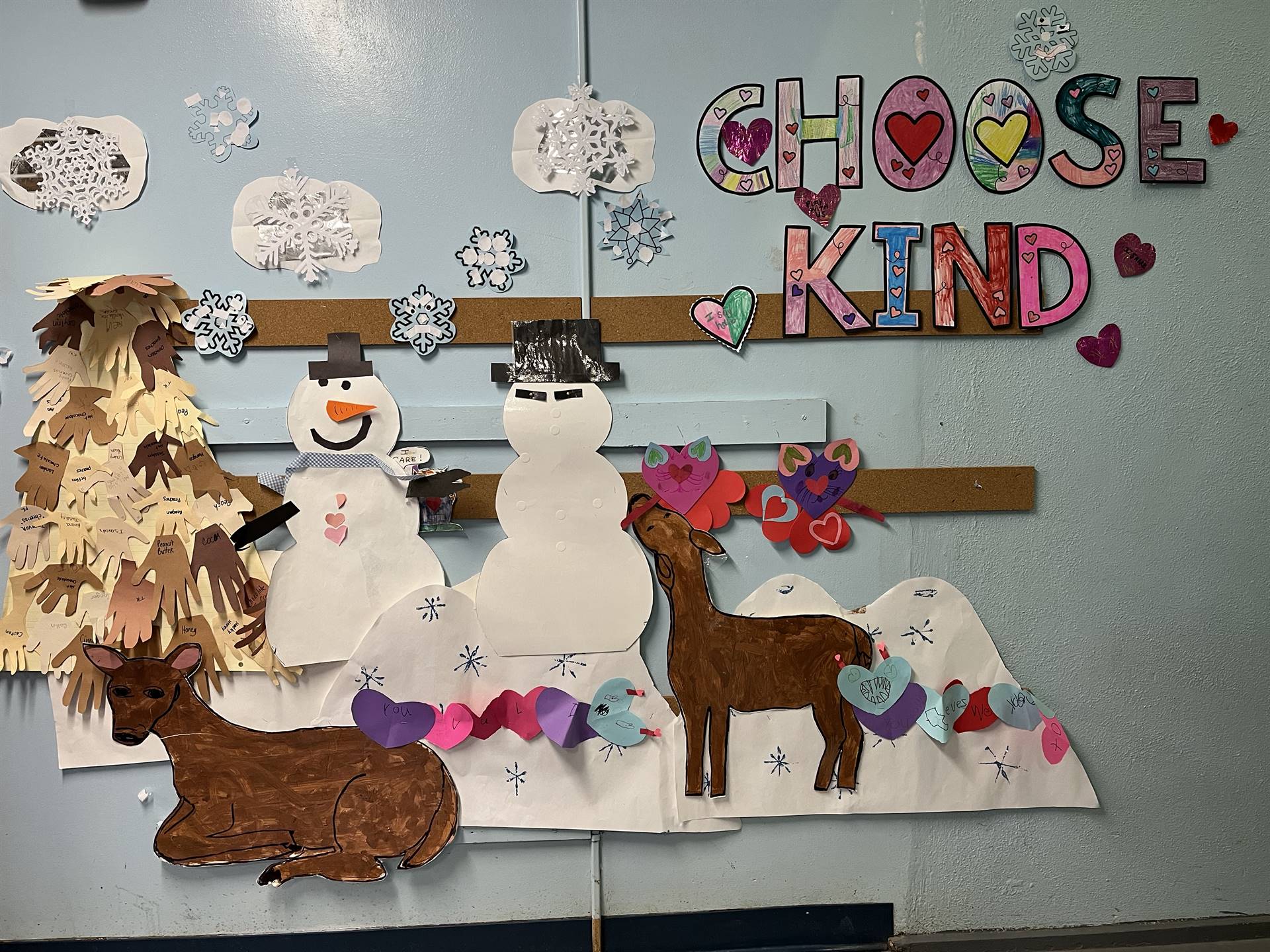 Letters CHOOSE KIND with snowmen, deer, snow, and a tree out of hands.