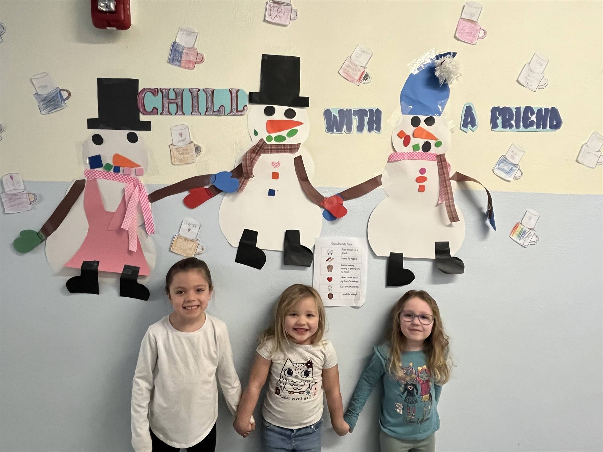 3 students hold hands with 3 snow friends on wall behind them