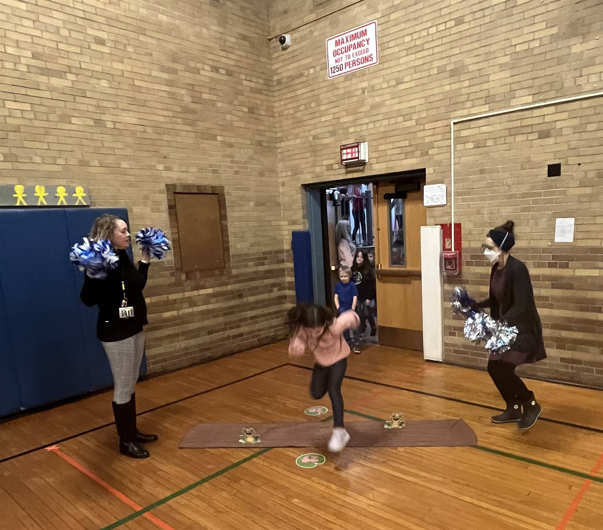 student between 2 adults leaping over a paper log.