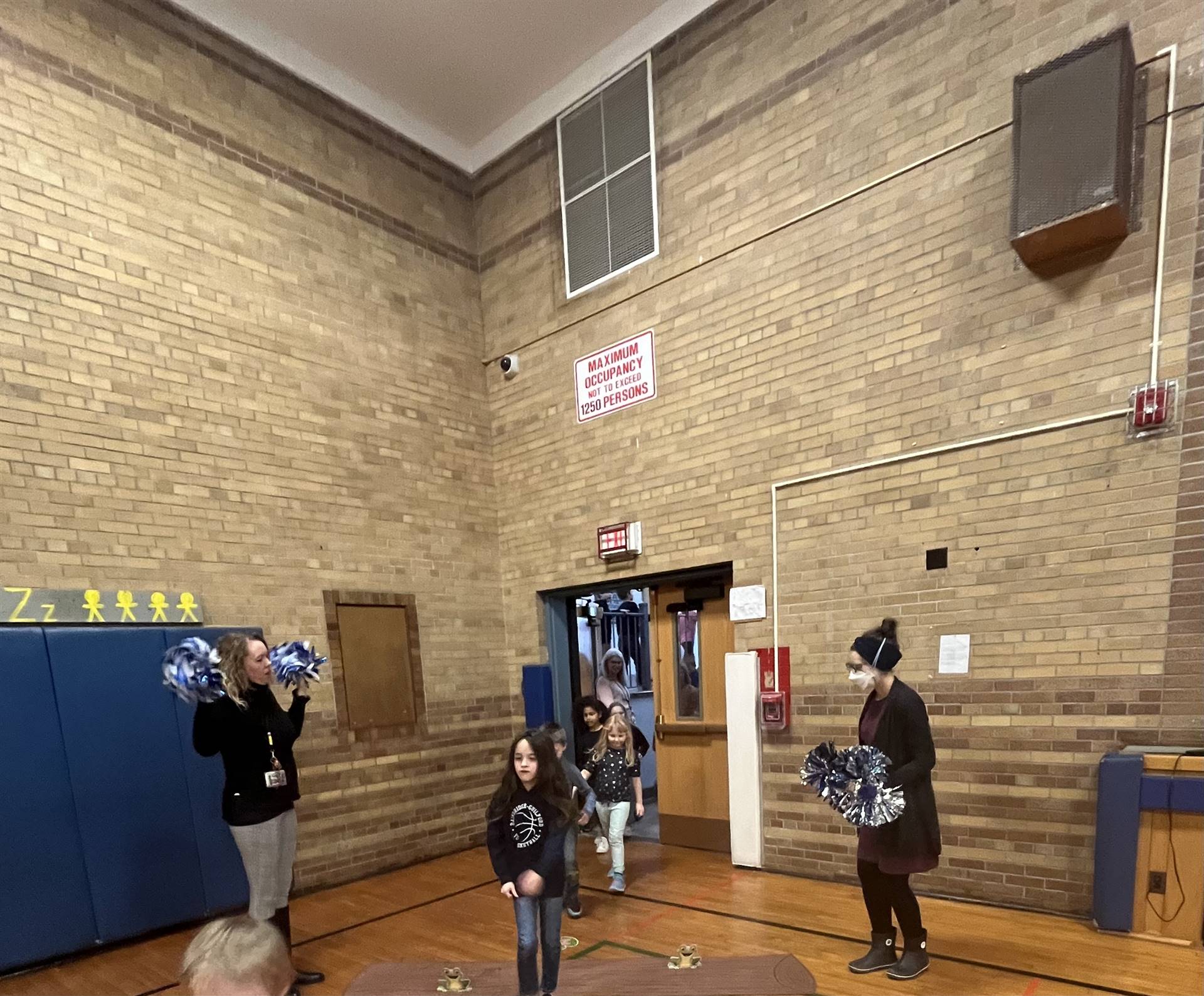 student between 2 adults leaping over a paper log.