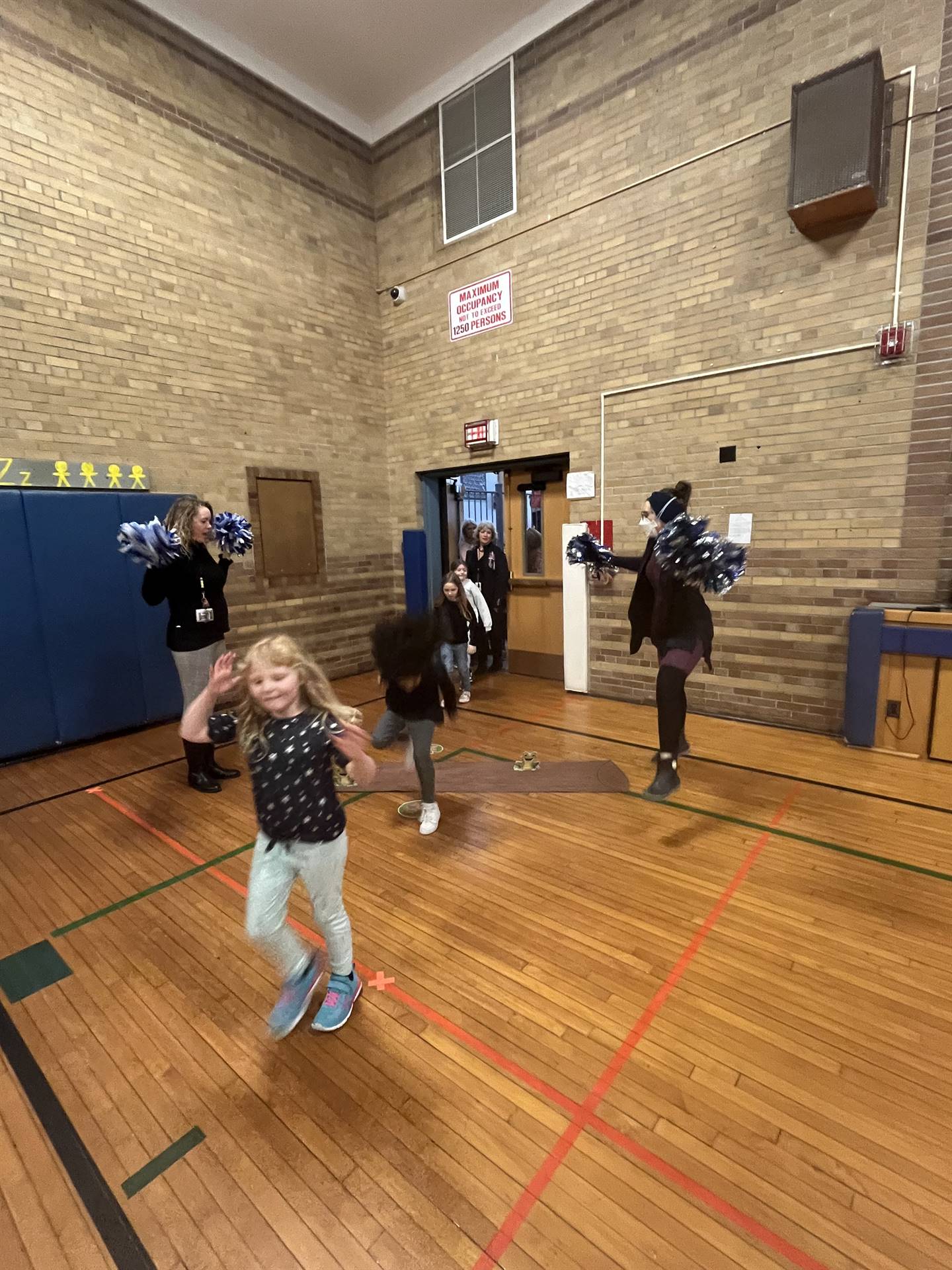 student between 2 adults leaping over a paper log.