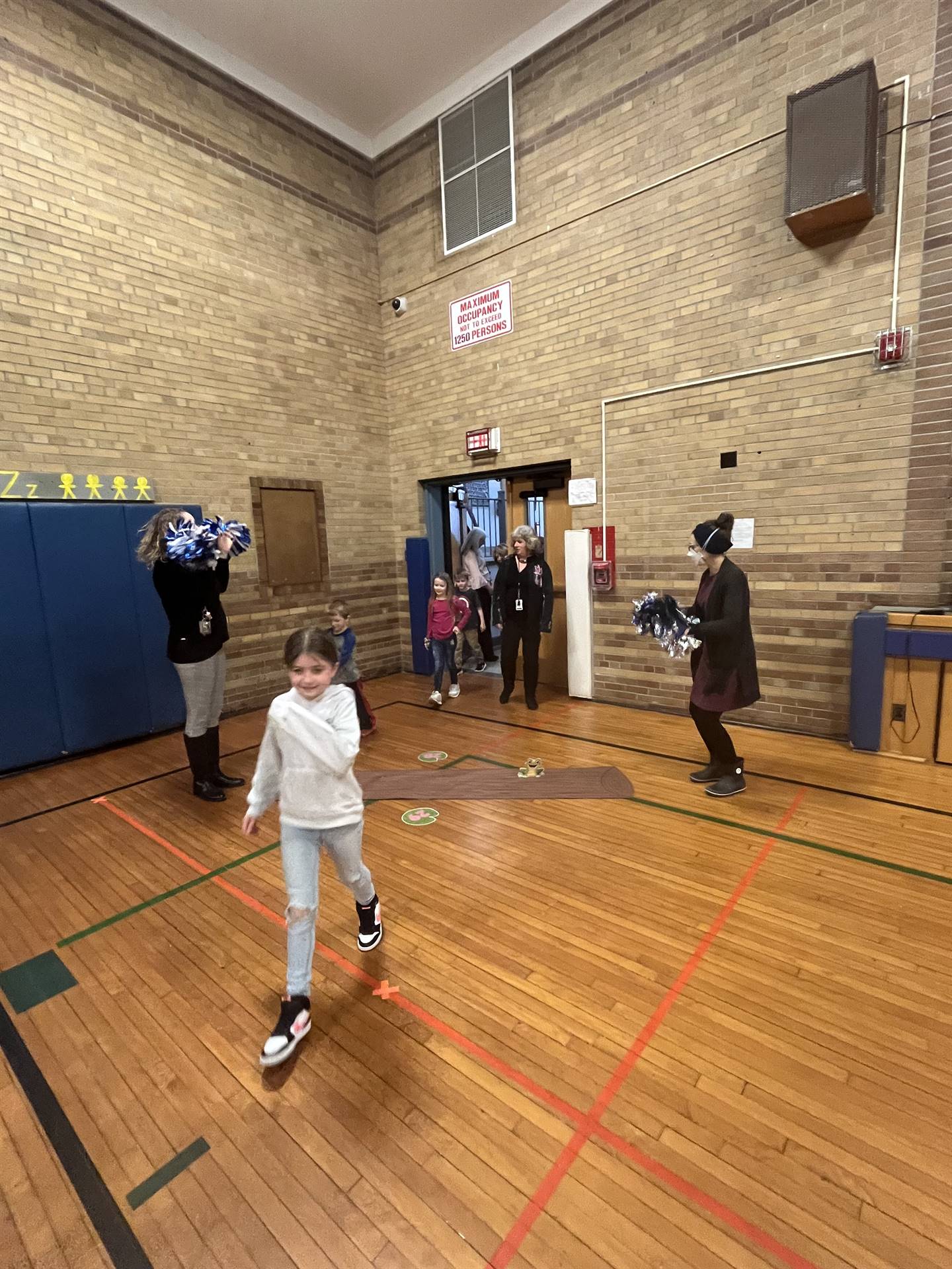 student between 2 adults leaping over a paper log.