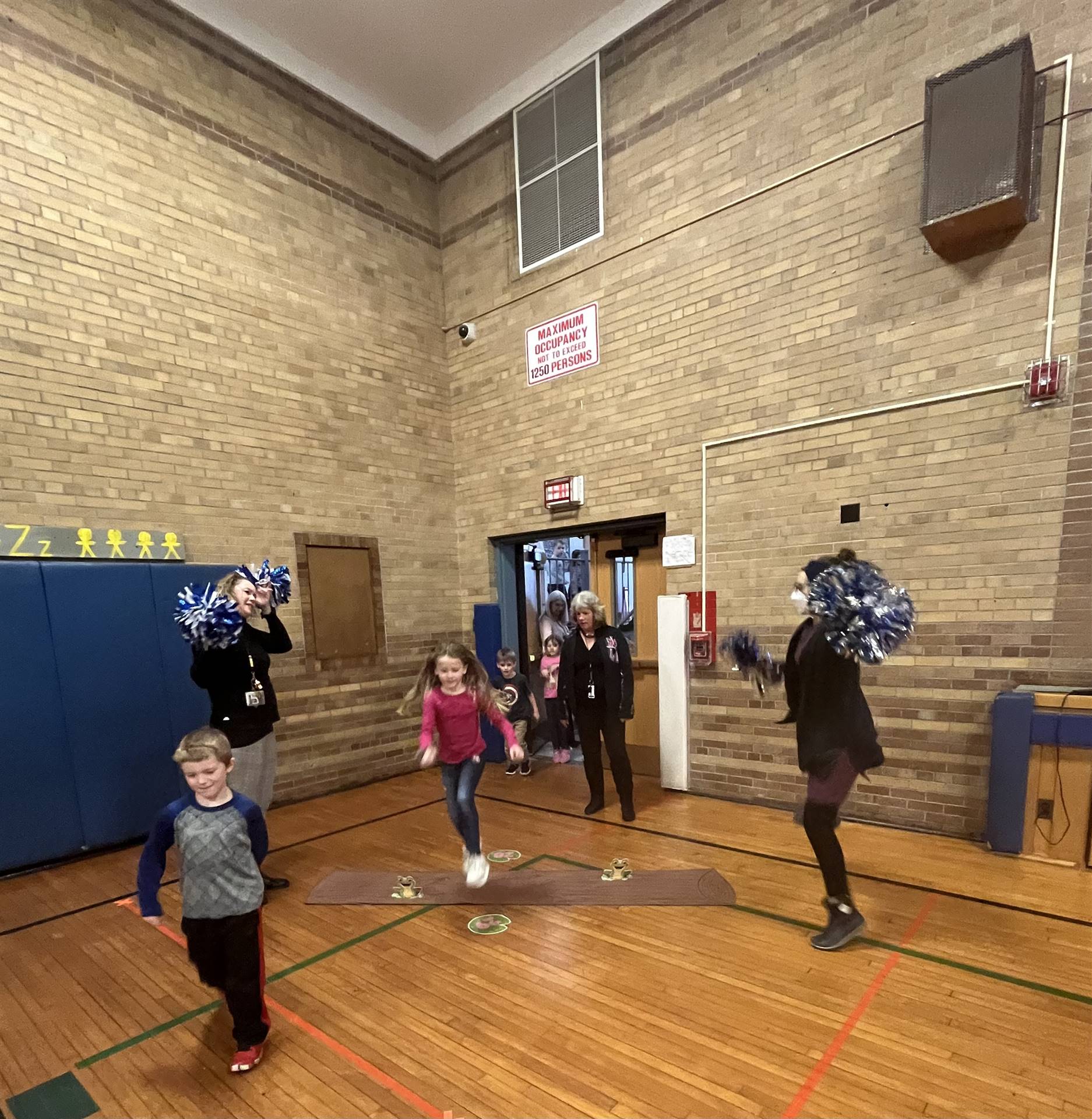 student between 2 adults leaping over a paper log.