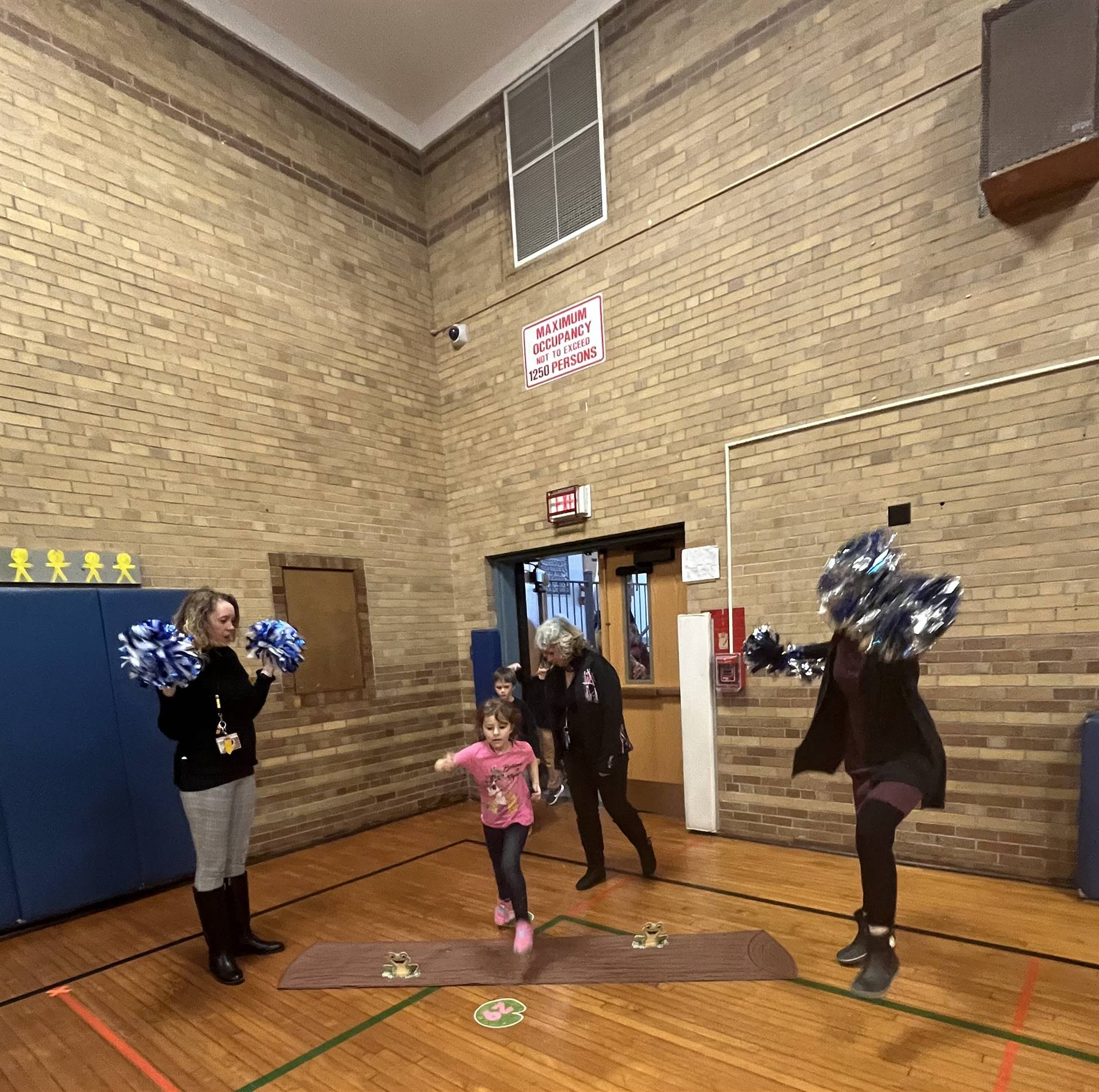 student between 2 adults leaping over a paper log.